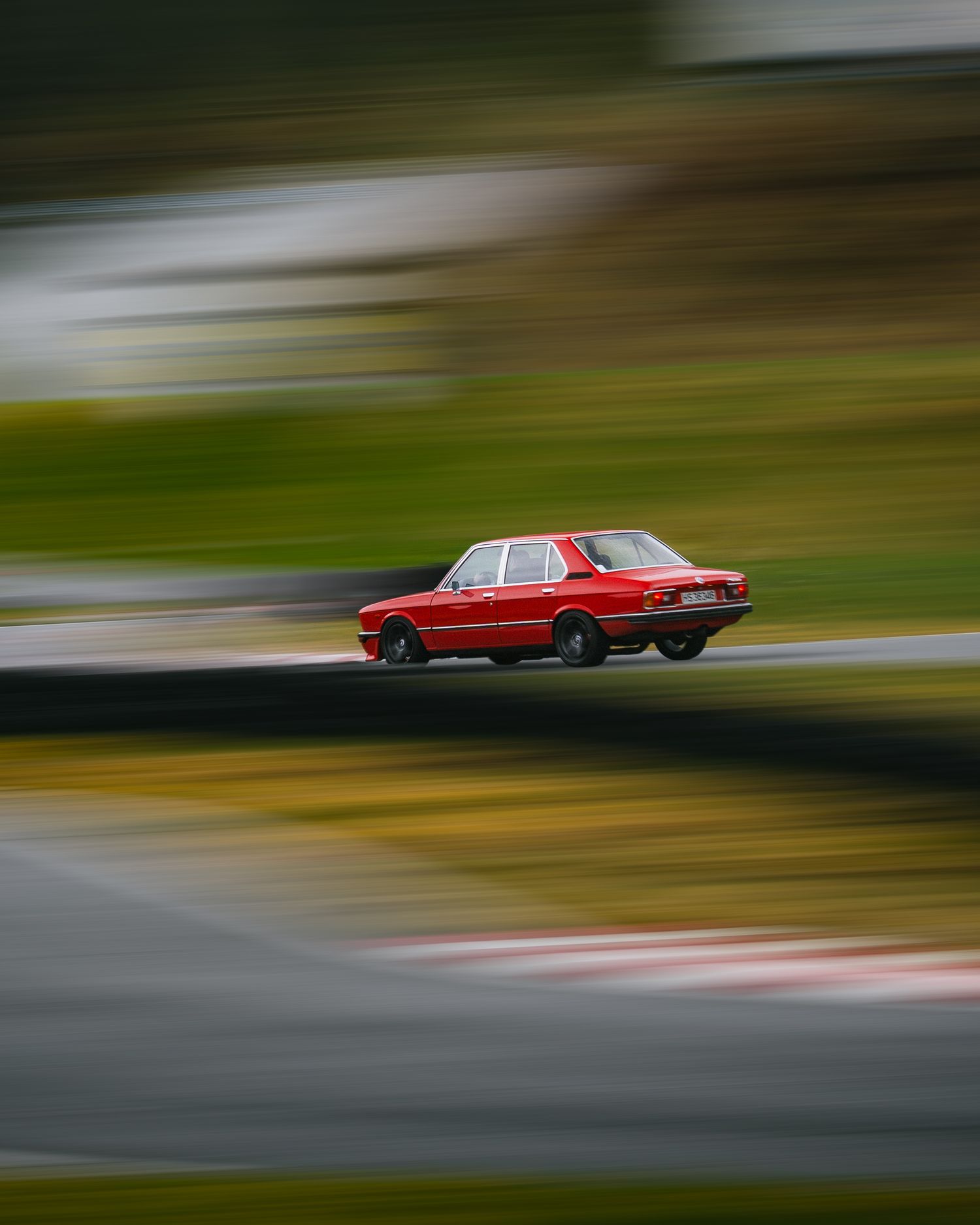 Red vintage car in motion on a racetrack with motion blur creating a dynamic speed effect.
