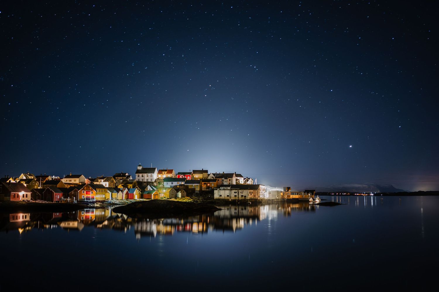 Scenic nighttime panorama of a waterfront town with glowing lights reflecting on the harbor.