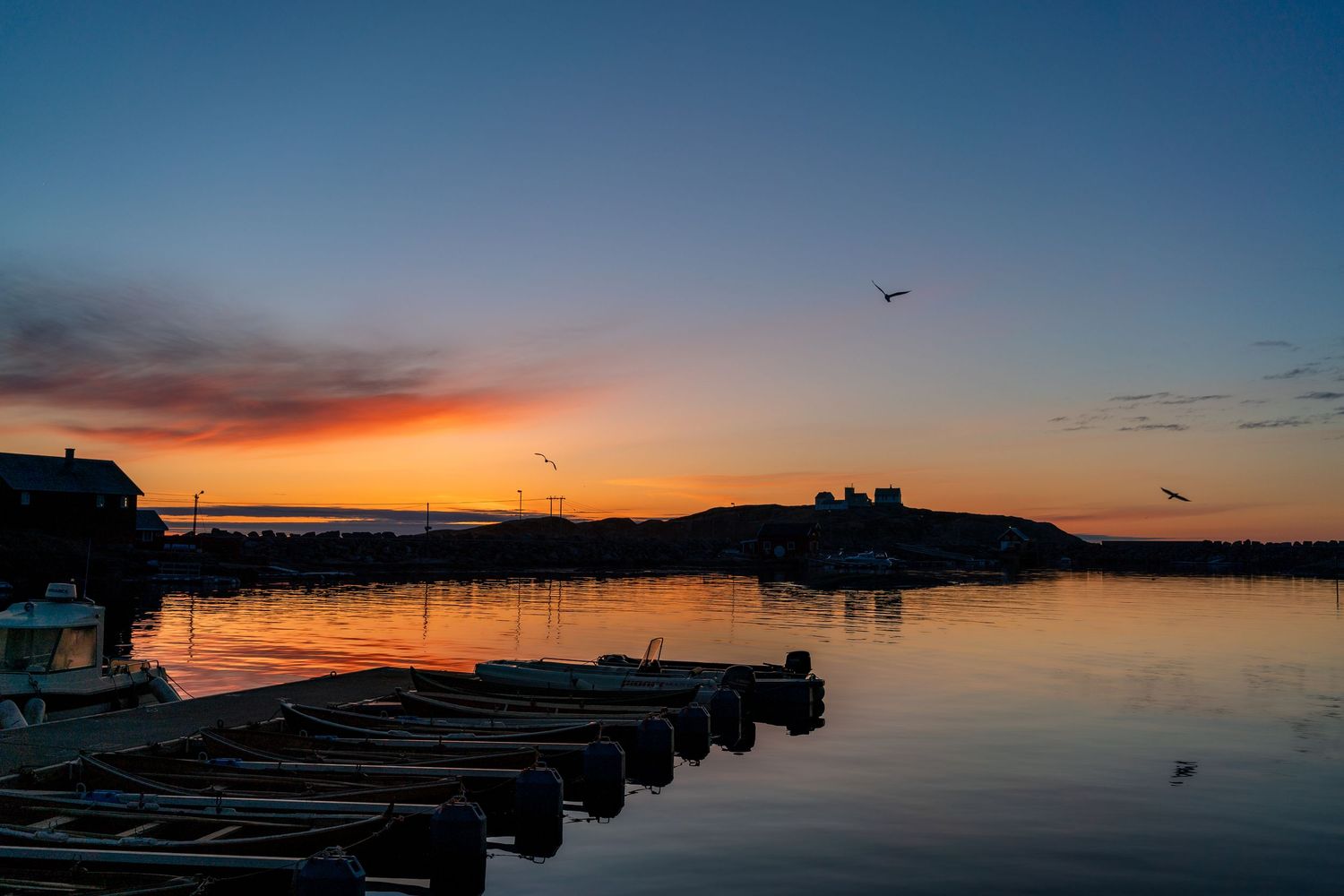 Sunset silhouettes docks and boats against colorful sky in Nordic harbor.