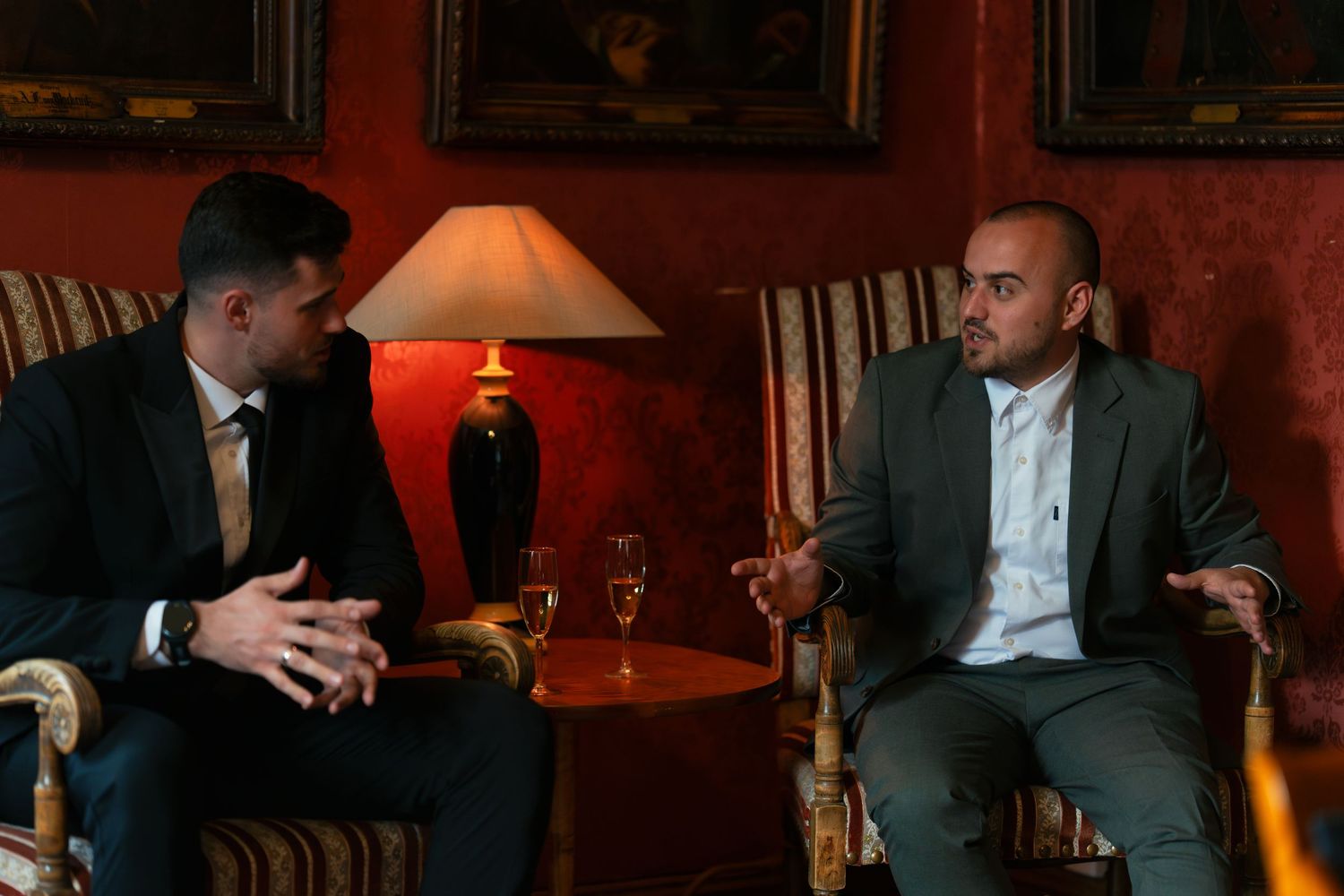 Two guests having an animated discussion while seated in elegant red-walled room.