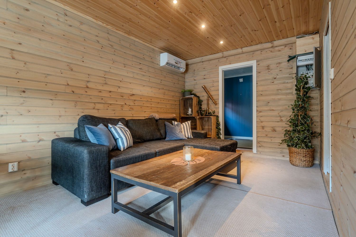 Modern cabin living room with wooden walls, black leather sofa, and industrial coffee table under recessed lighting.