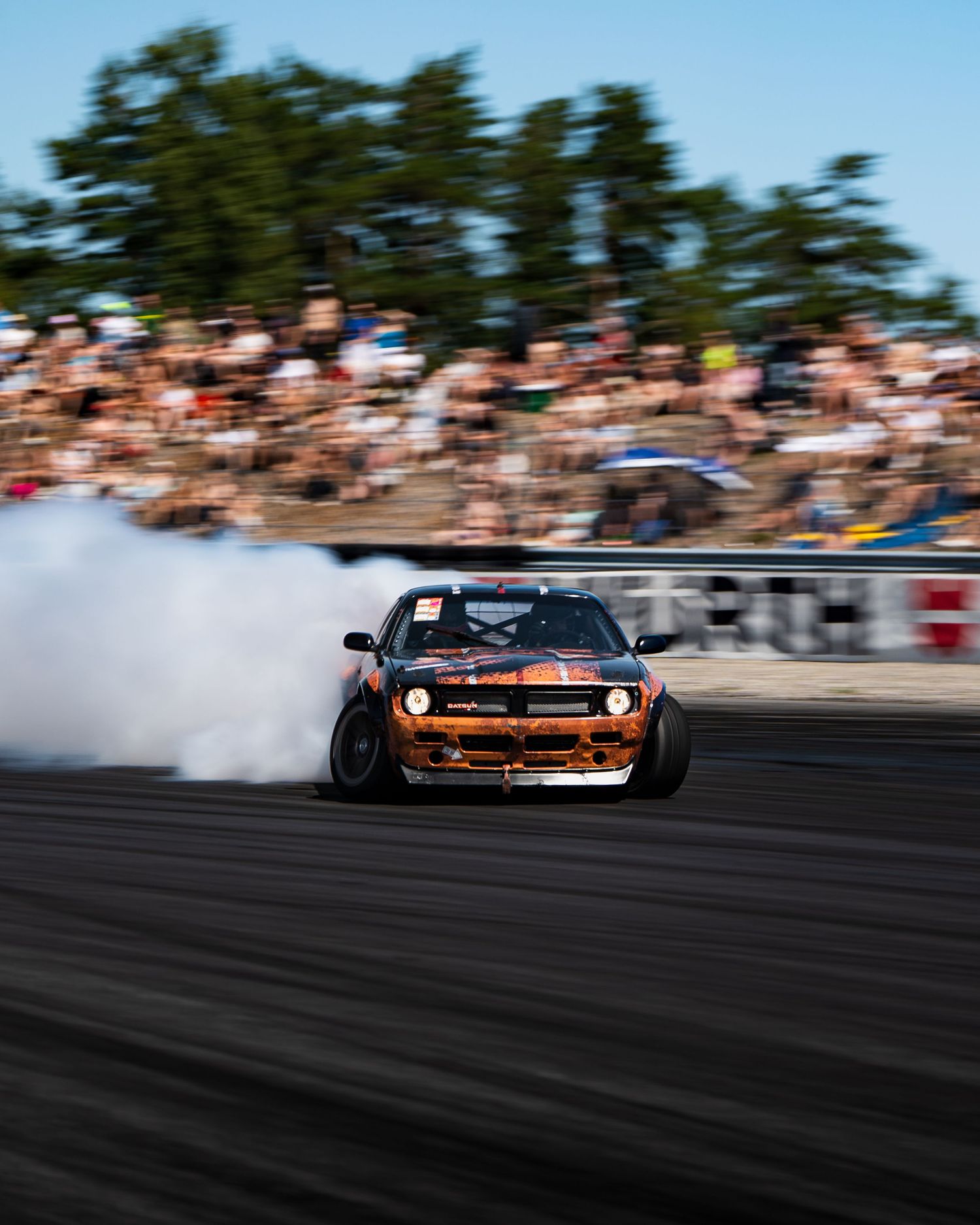 Orange sports car drifting on a racetrack with smoke trails and spectators visible in the background.