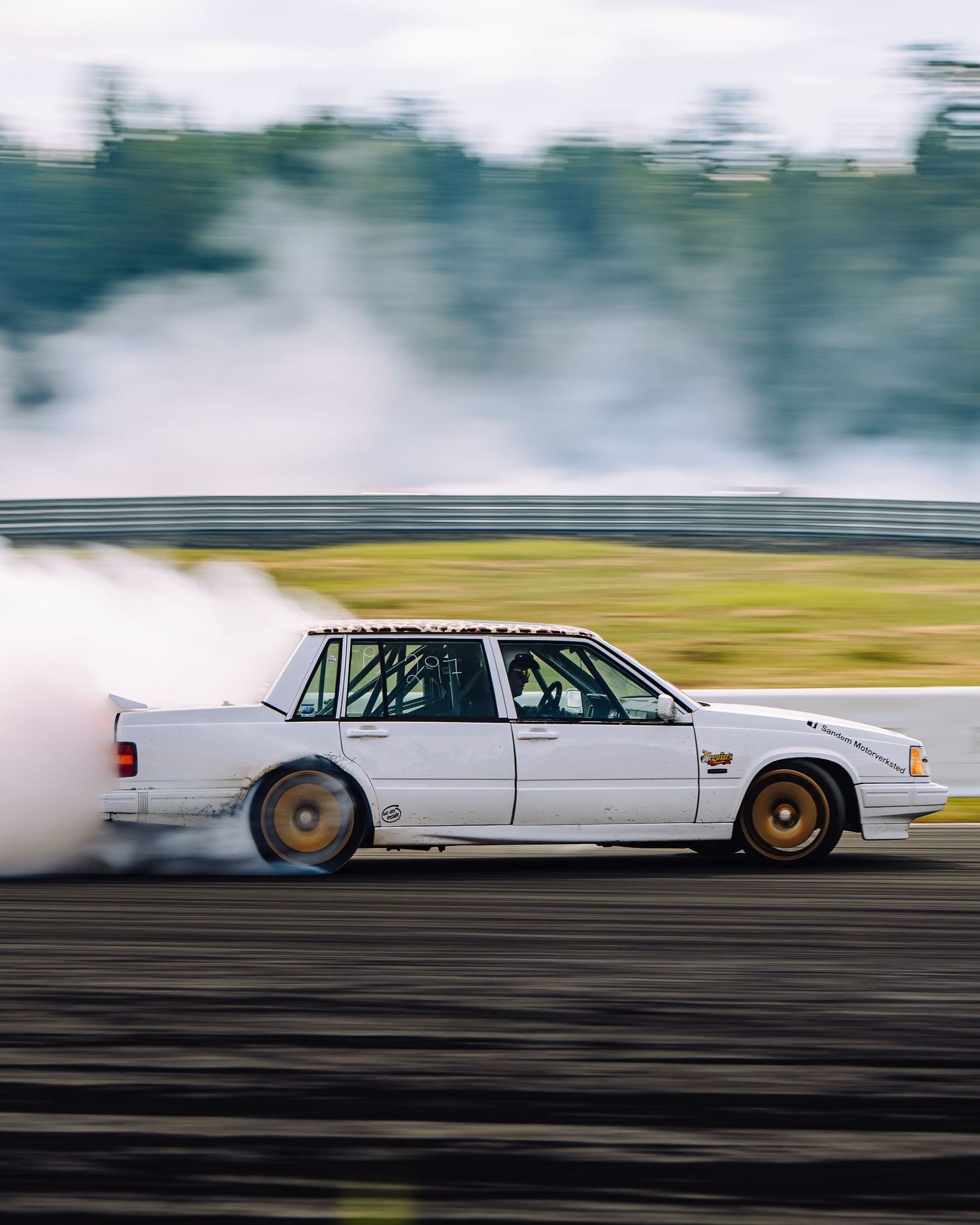 White classic car drifting on a race track creating smoke during a motorsport performance.