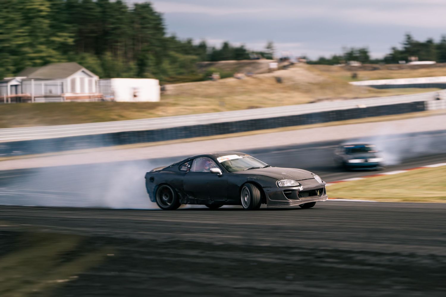 Sports car drifting on a racetrack creating smoke from burning rubber during high-performance driving maneuvers.