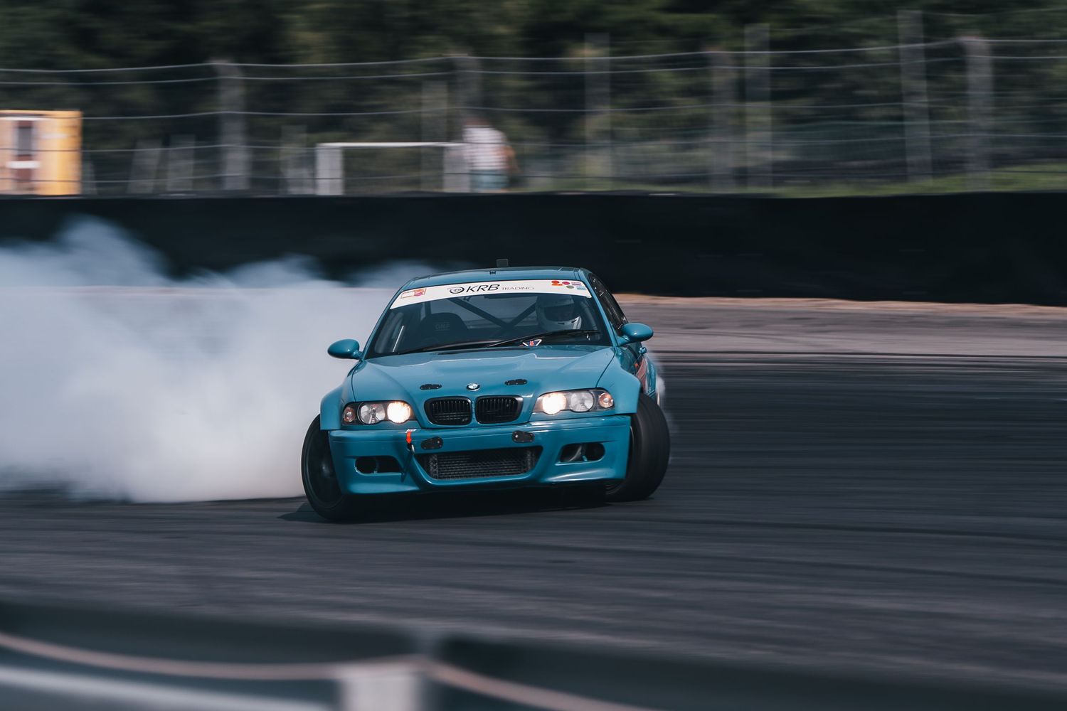 A blue BMW M3 drifts around a racetrack with smoke trailing from its tires during a performance driving session.