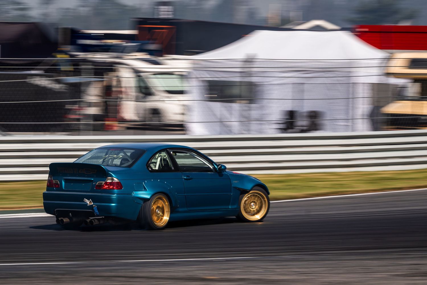 Blue modified sports car drifting on racetrack with gold wheels and motion blur effect.