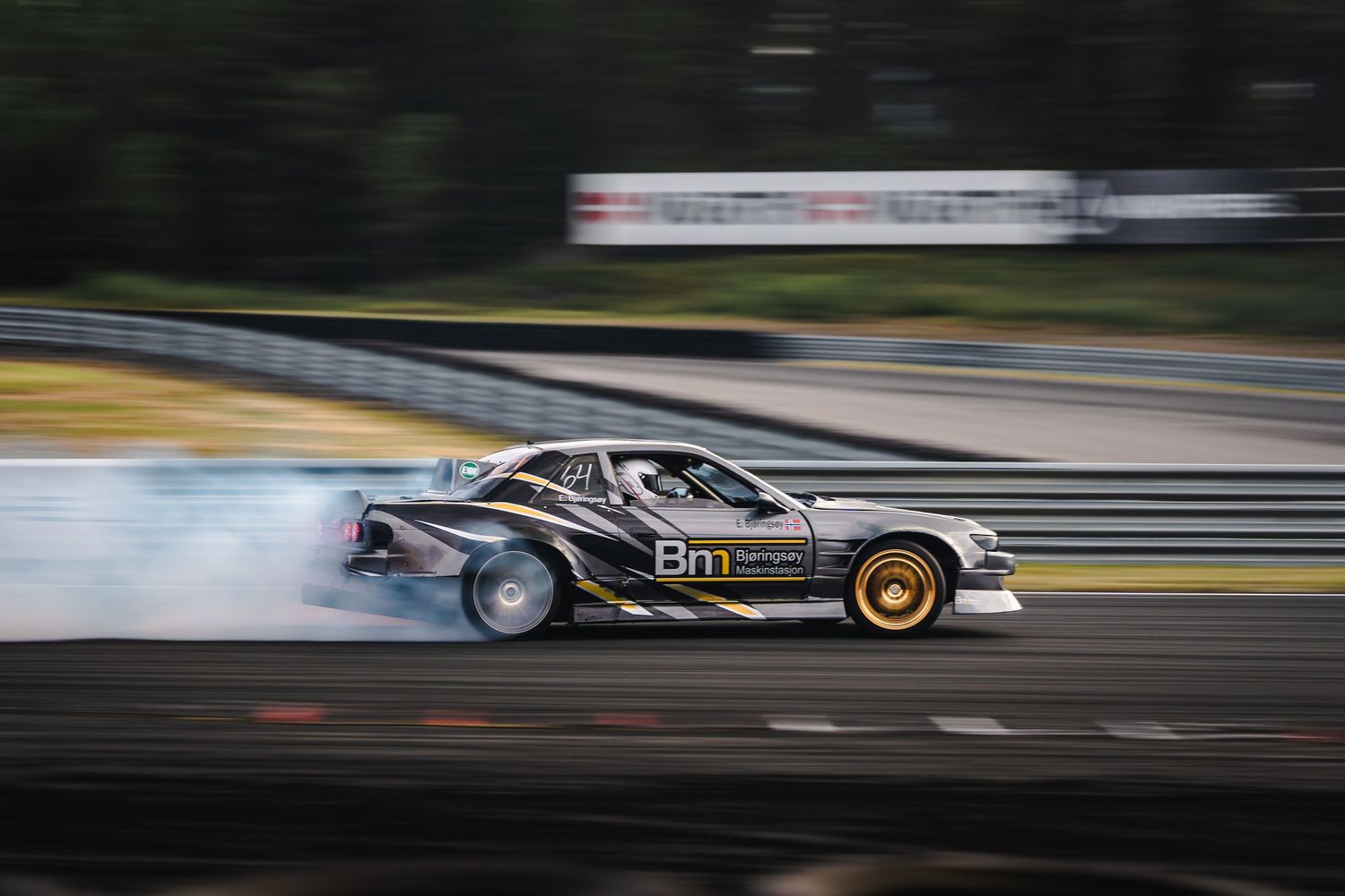 A drift car slides sideways on a race track creating smoke while in motion during a competition.