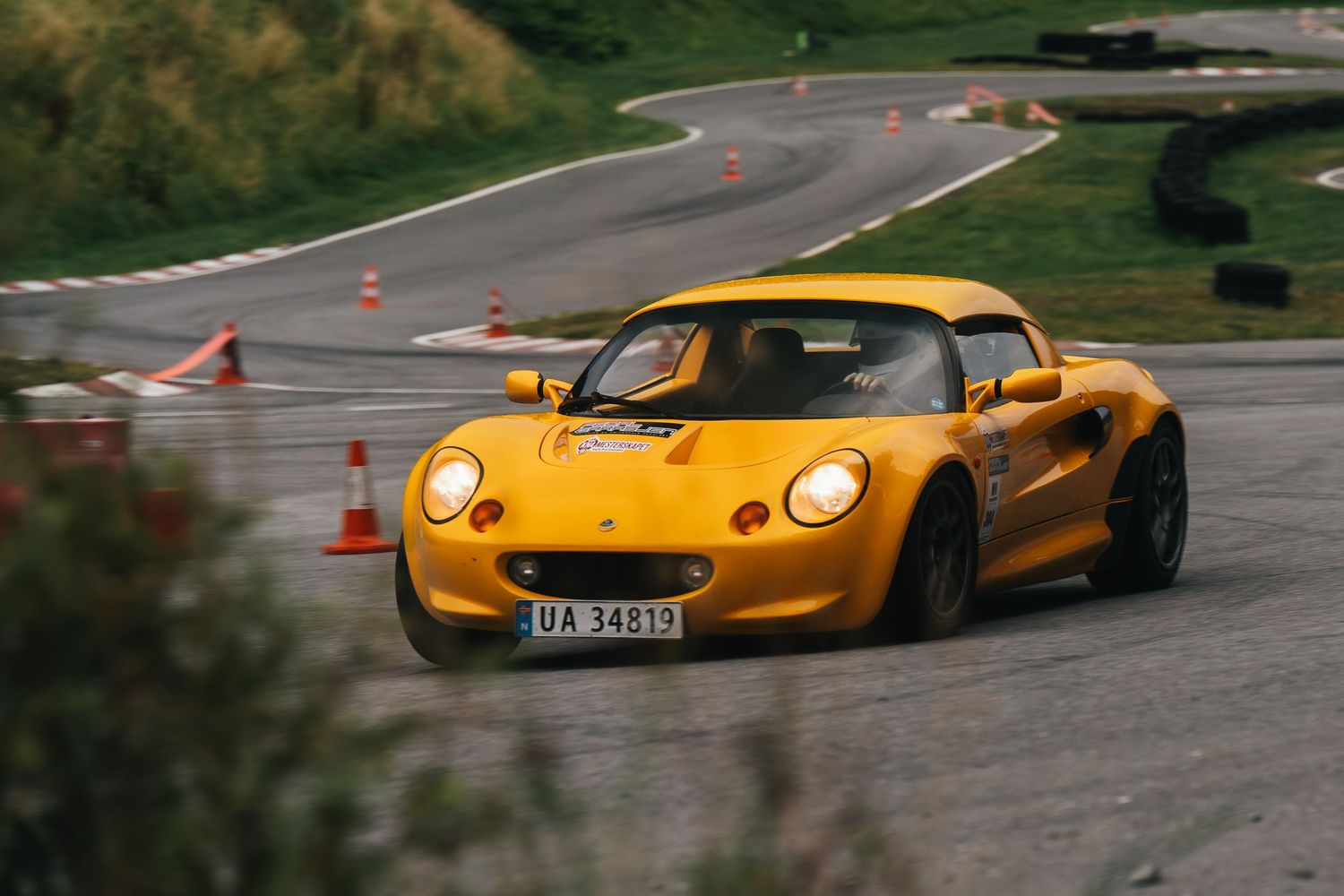Yellow Lotus Exige sports car racing around a track with orange cones marking the course.