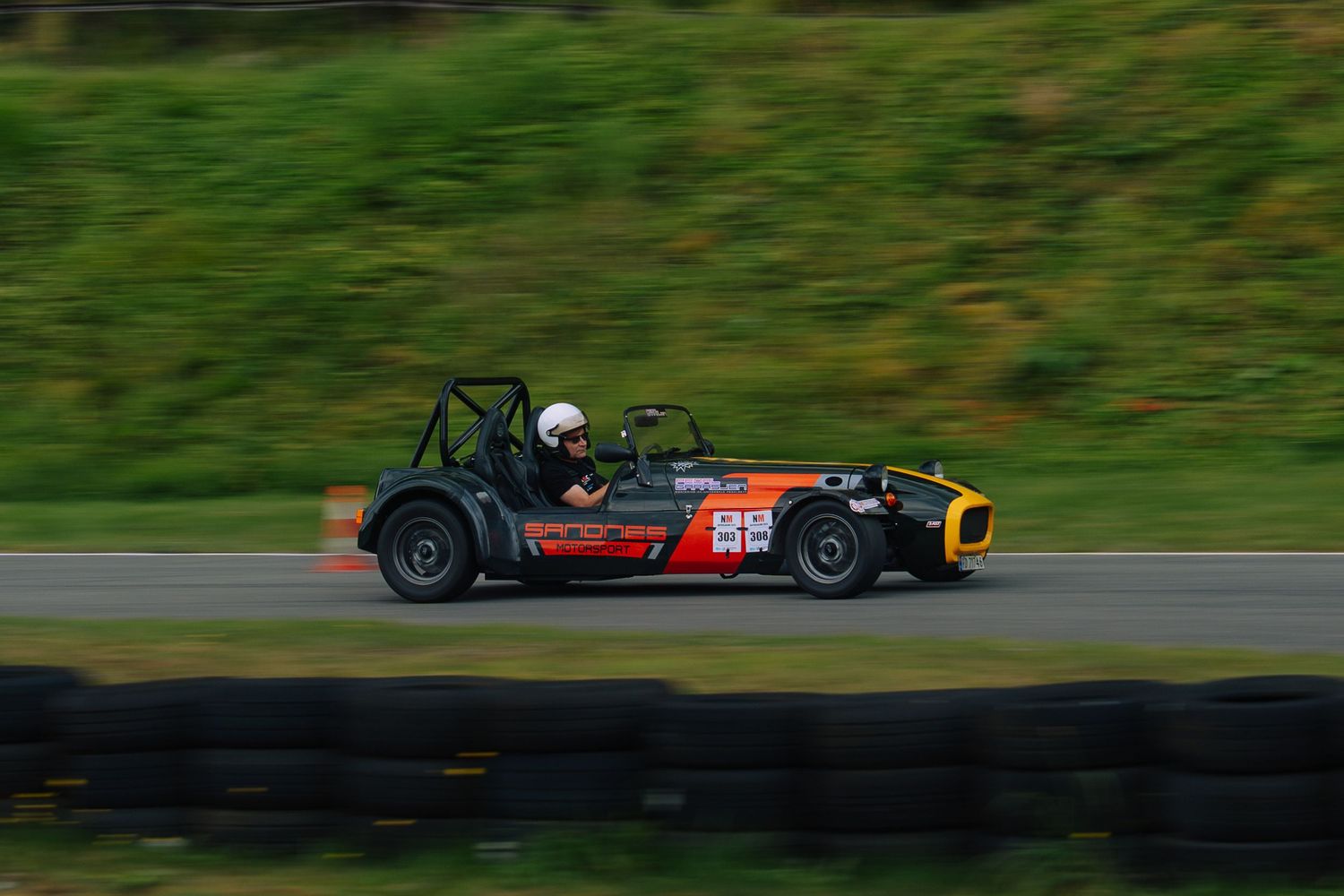 Black formula race car with red number 89 speeds around a racetrack with green background.