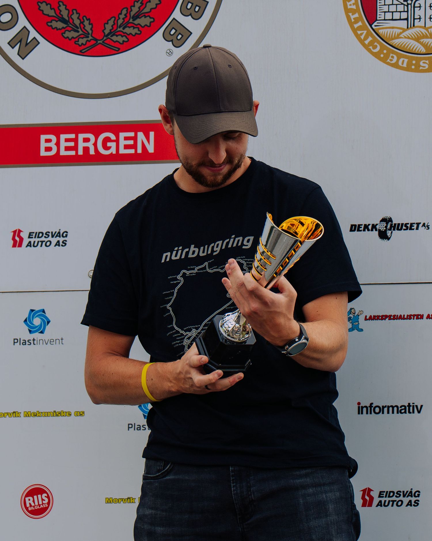 Someone in a Nurburgring t-shirt examines a trophy while standing in front of a wall with sponsor logos.