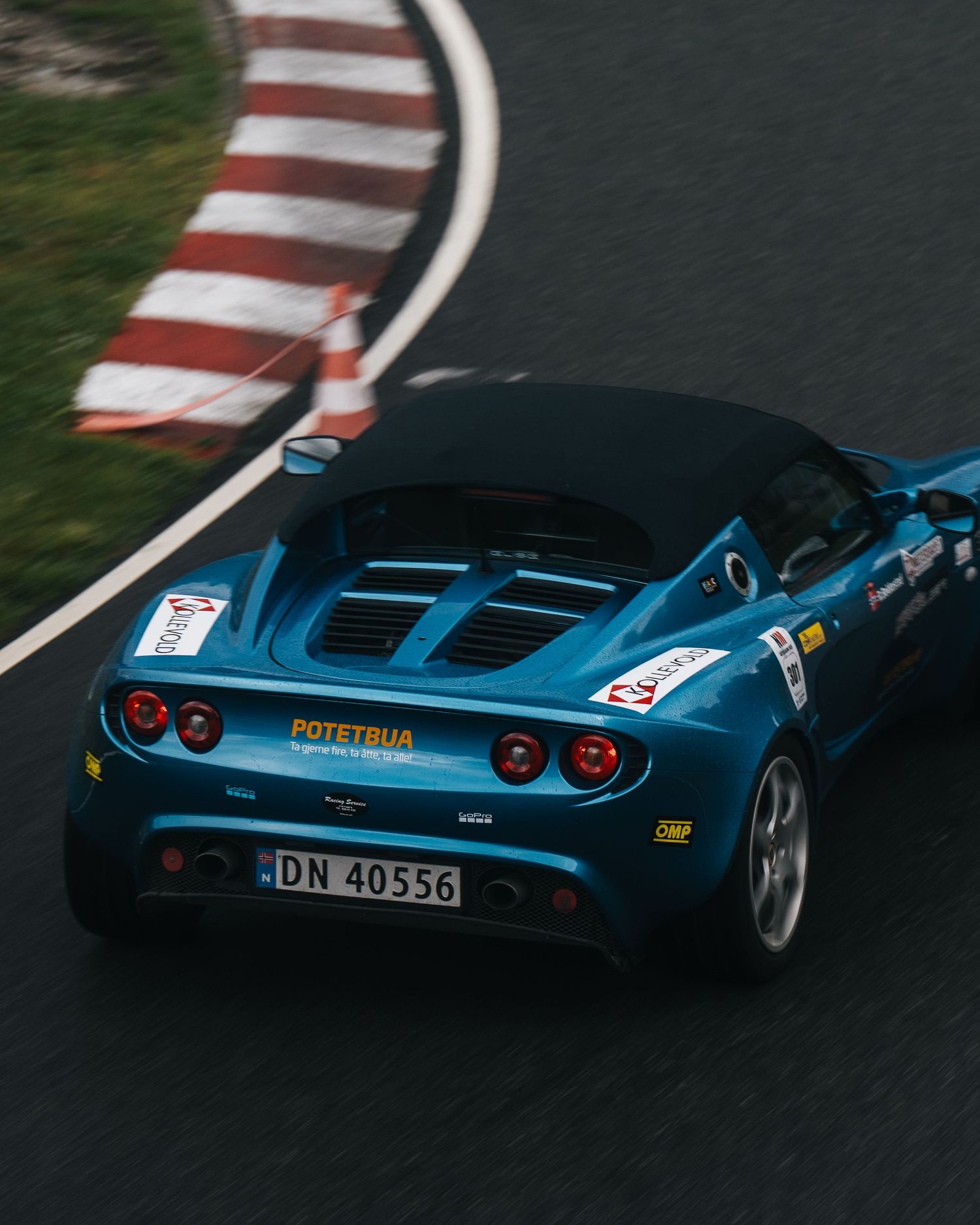 A blue sports car navigates a curvy racetrack with red and white striped barriers visible in multiple angles.