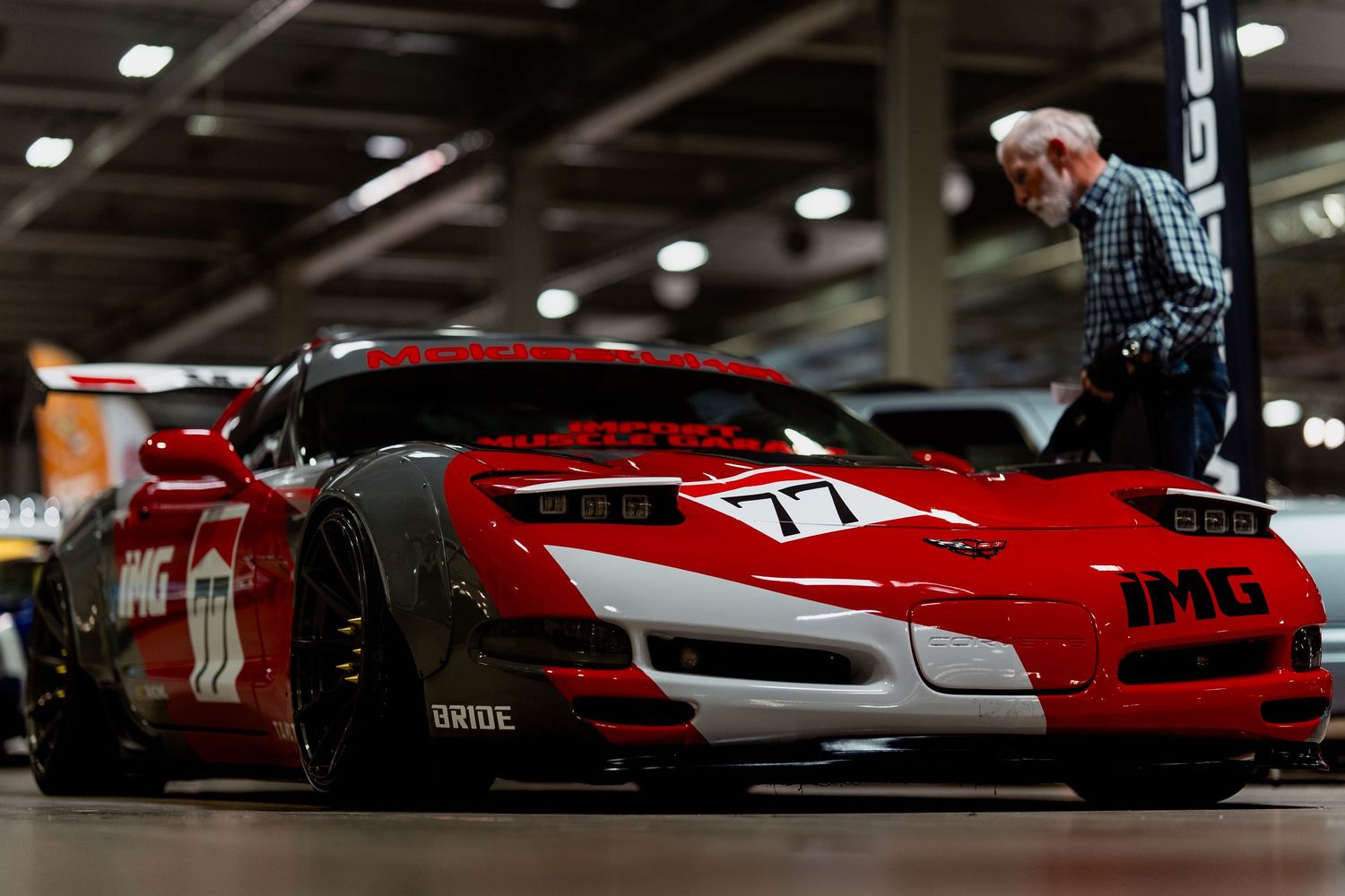 Modified red sports car with aggressive body kit and racing livery displayed in indoor exhibition space.