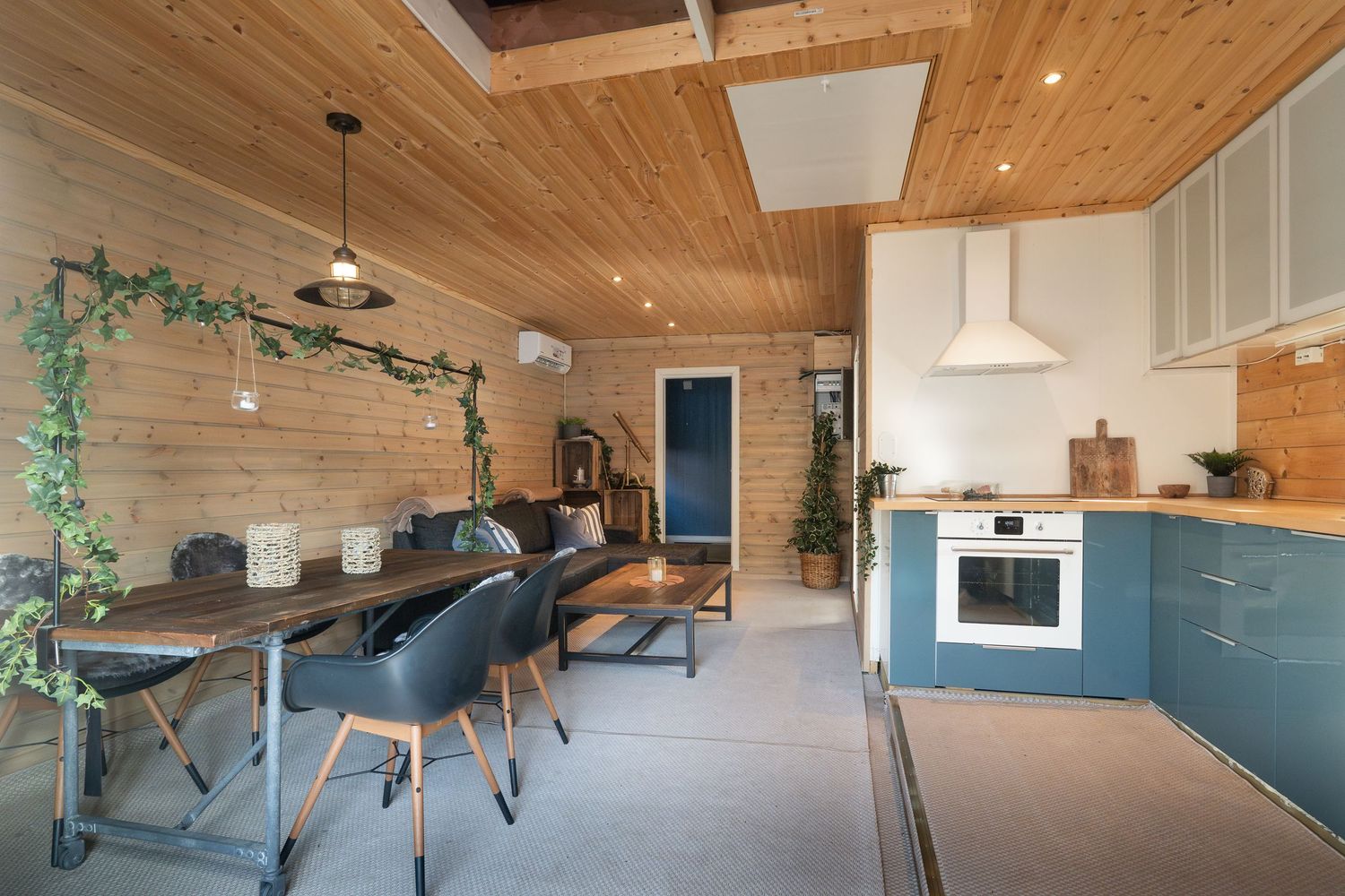 Open concept dining and kitchen space with teal cabinets, wooden ceiling, and modern furnishings.