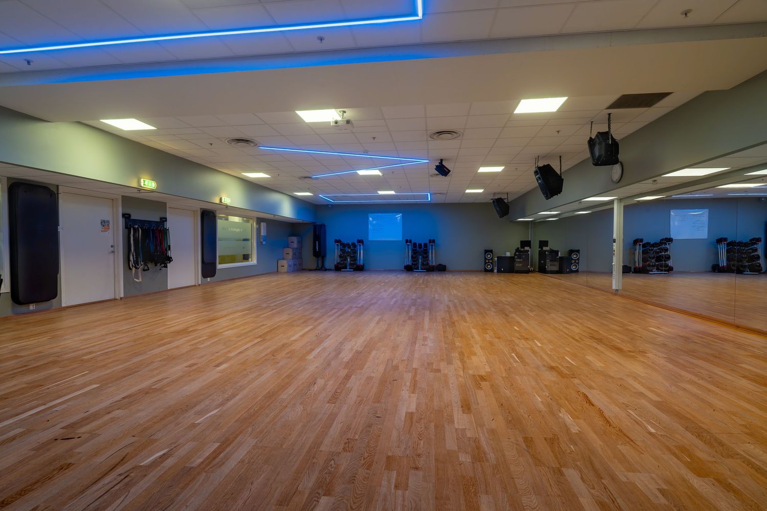 Large dance studio with wooden floors, mirrored walls, and blue accent lighting along the ceiling.