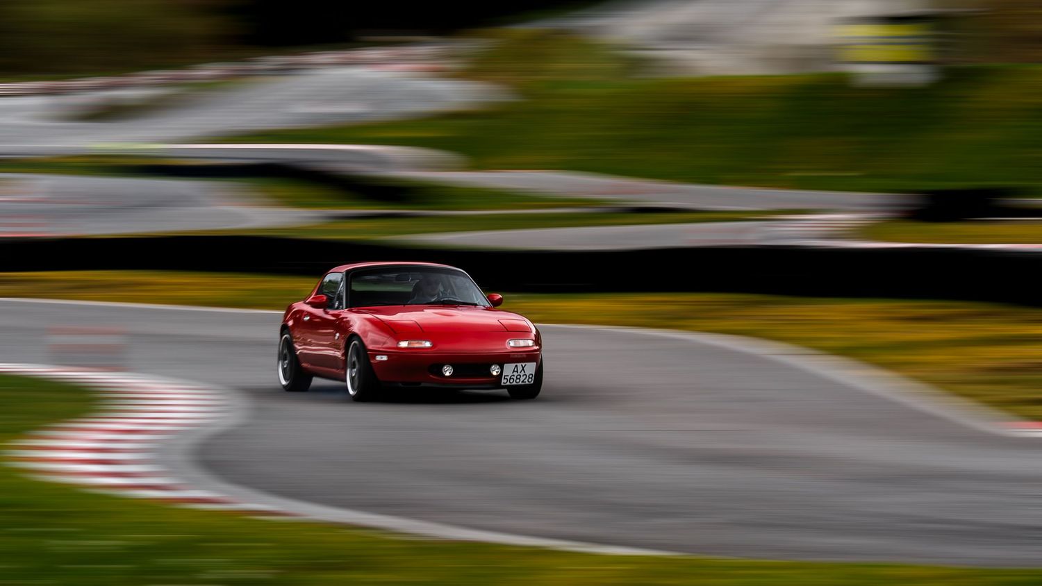 Red sports car speeds through a winding racetrack with motion blur effect.