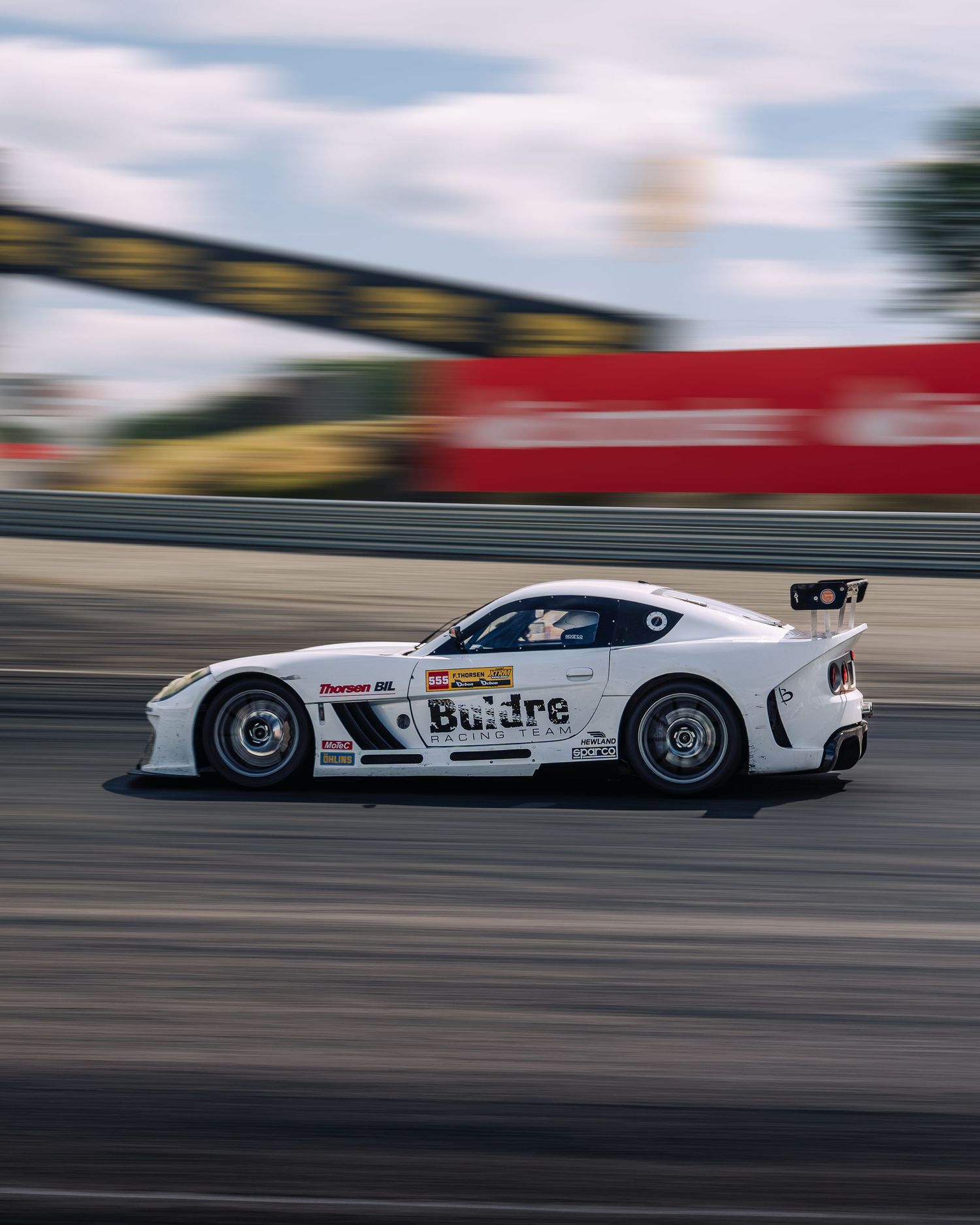 White racing car with Budre branding speeding across a track captured in motion blur effect.