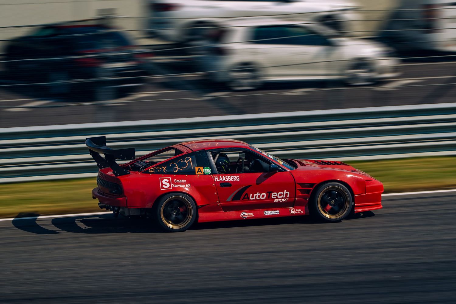Red racing car speeds along racetrack curve during competitive motorsport event.