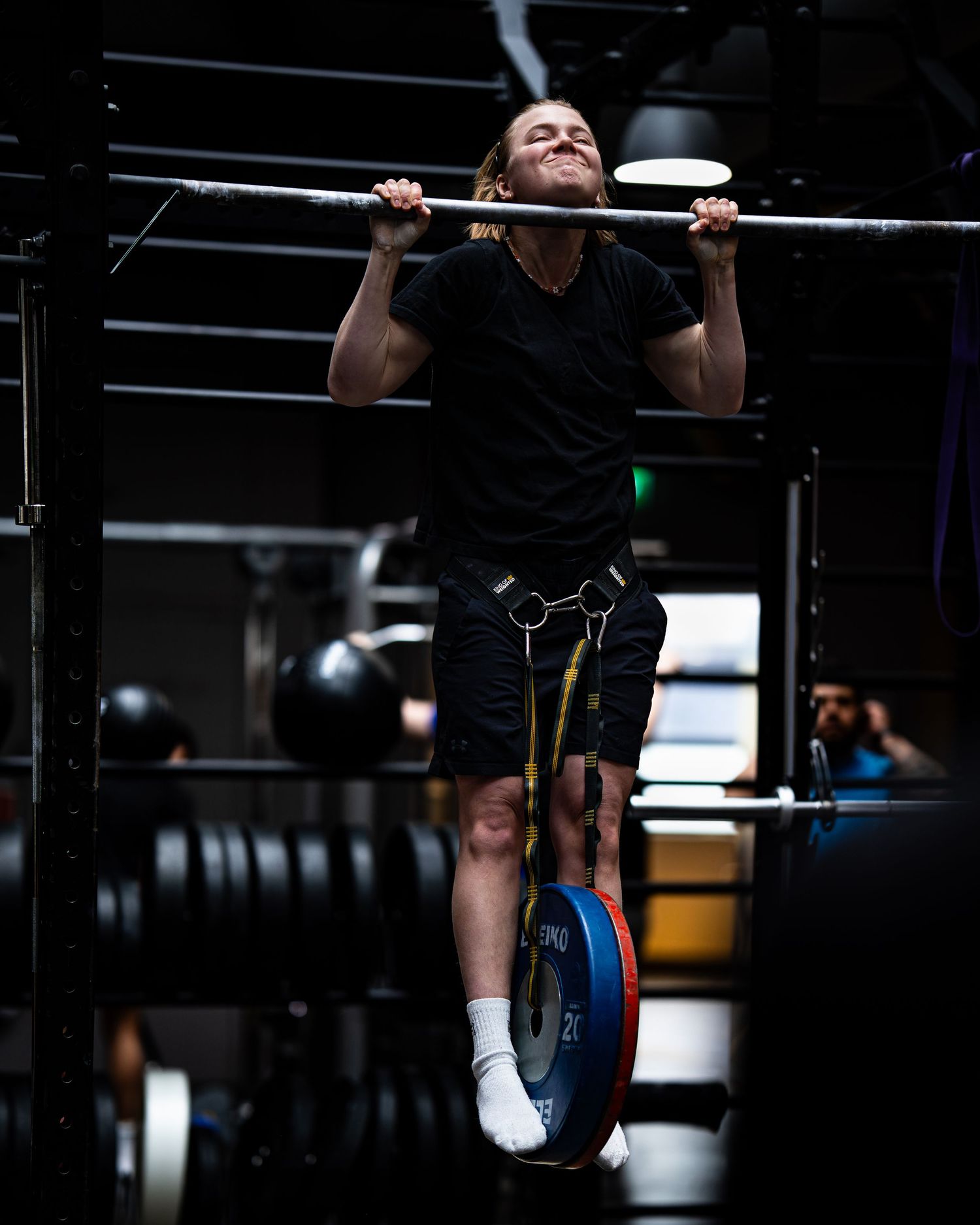 Athletes exercising on pull-up bars in a dimly lit CrossFit gym.