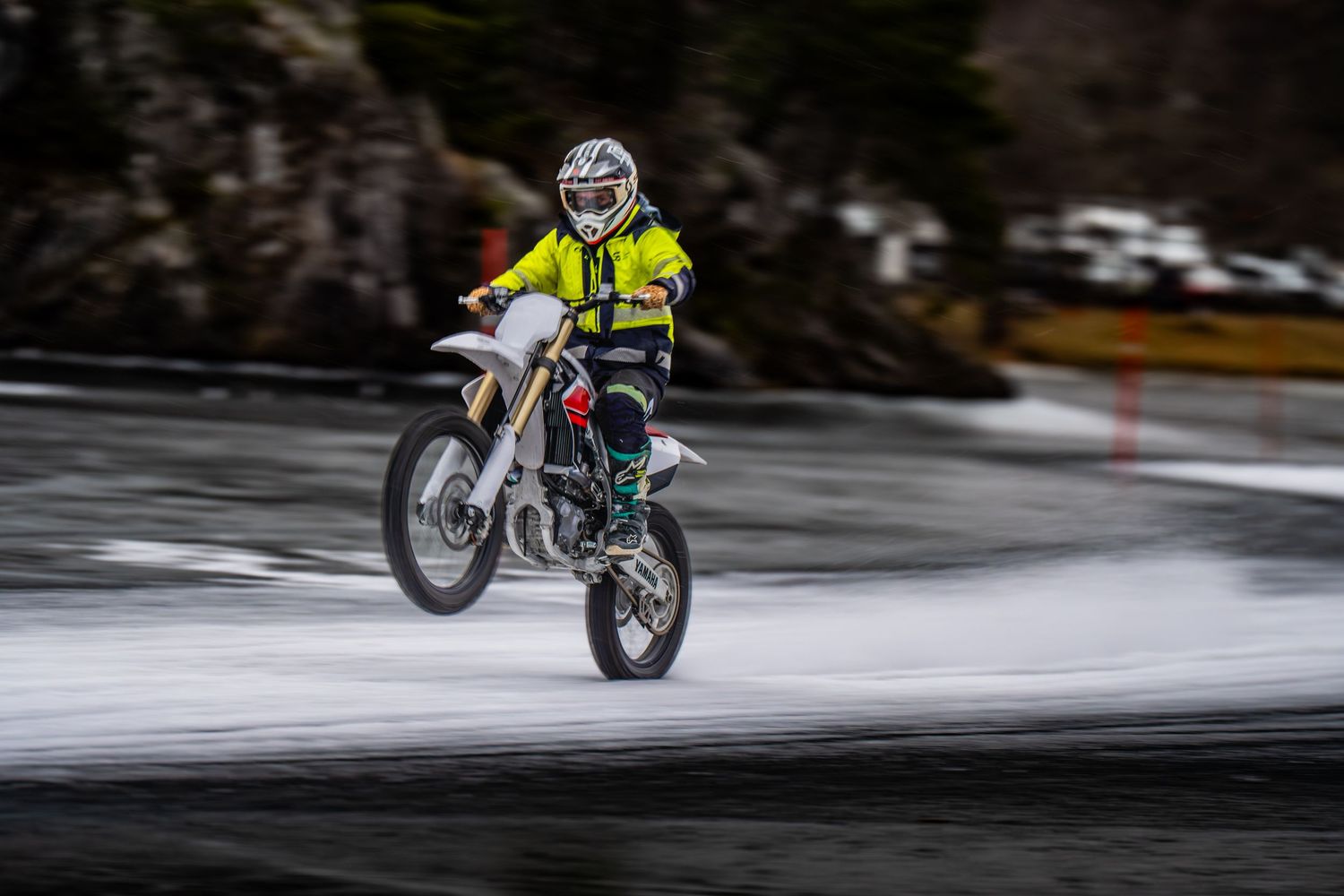 Dirt bike rider in bright yellow jersey performing jump on snowy terrain with motion blur effect.