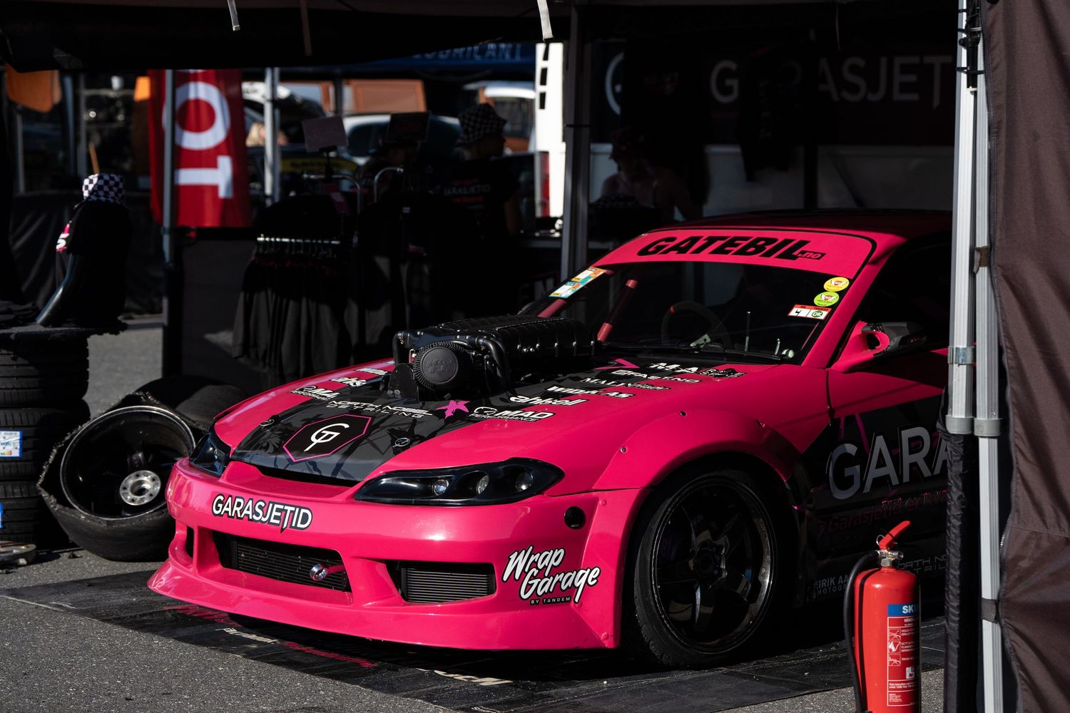 Pink sports cars line up at a racing event, showcasing sleek designs and performance modifications.