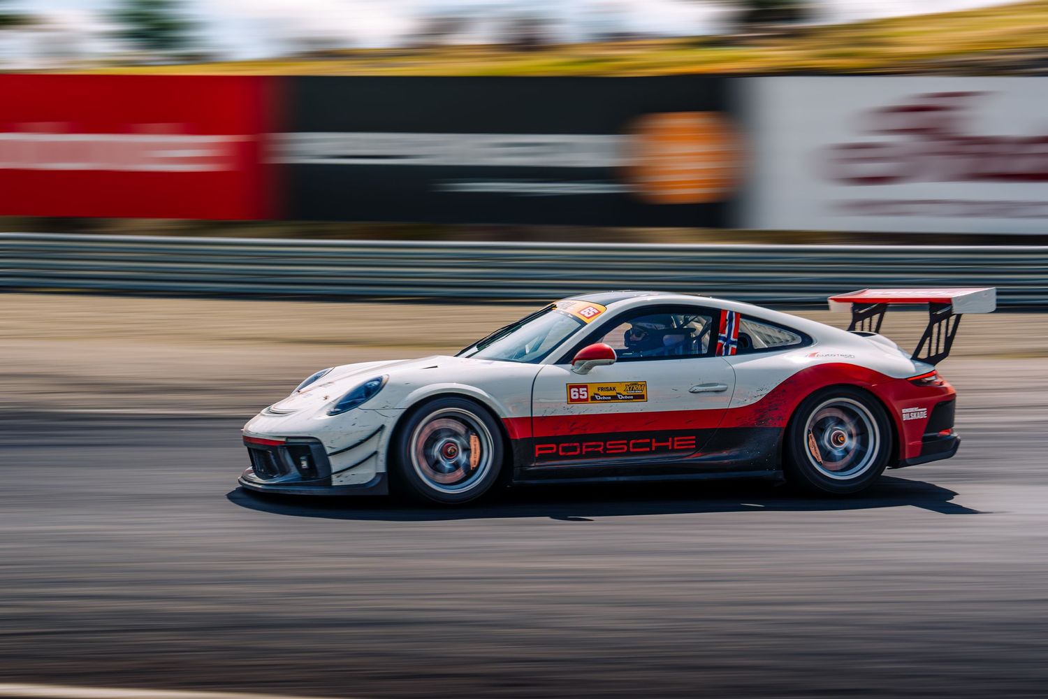 A white racing car with red and black accents speeds along a racetrack during a motorsport competition.
