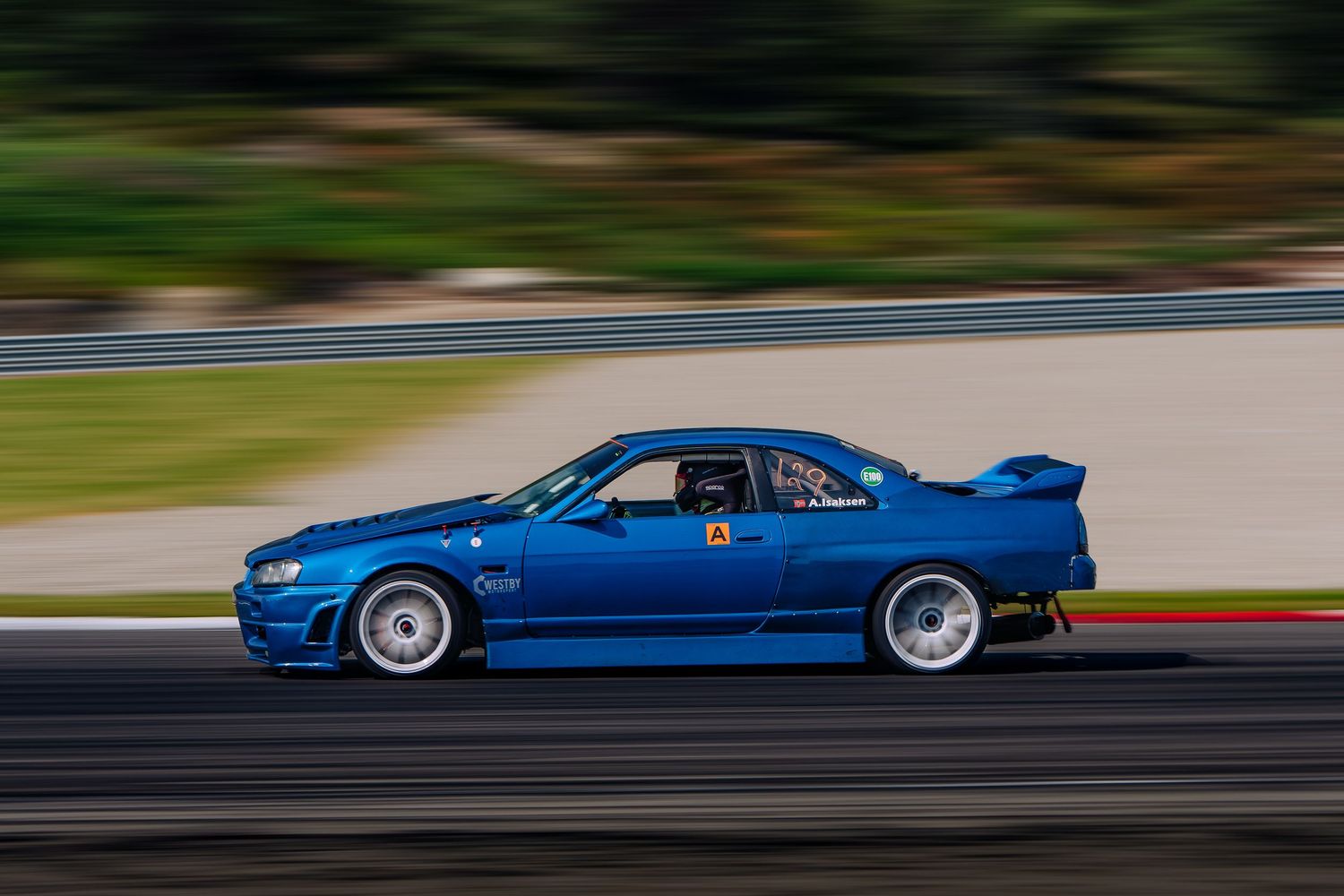 A bright blue sports car races along a track at high speed creating a dynamic motion blur effect.