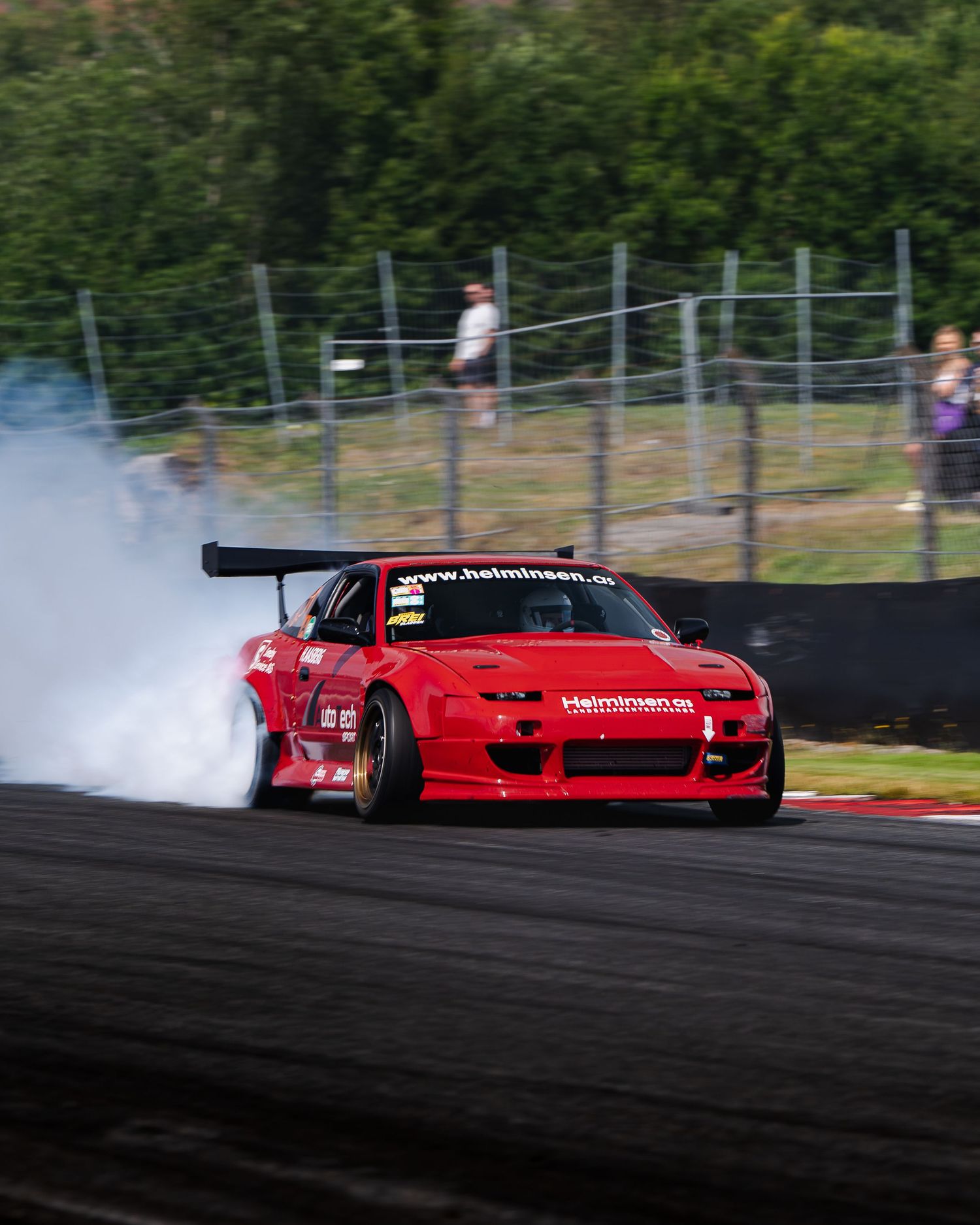 Red sports car drifting on a race track creating smoke while performing controlled slides.