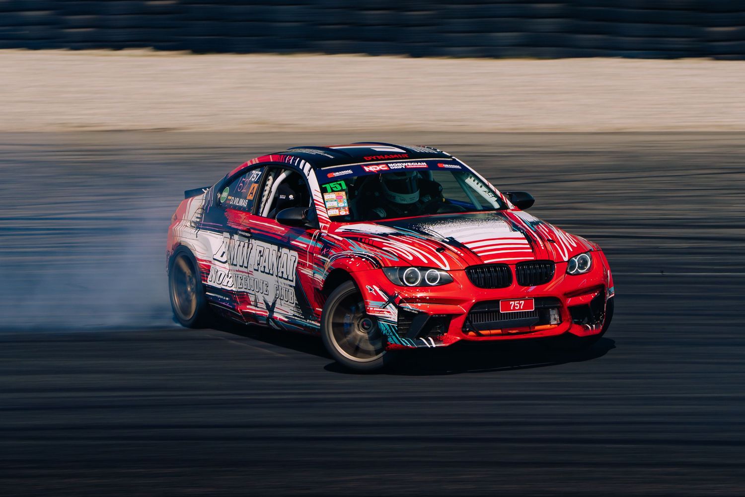 Red racing cars drift along a racetrack during a motorsport competition at sunset.