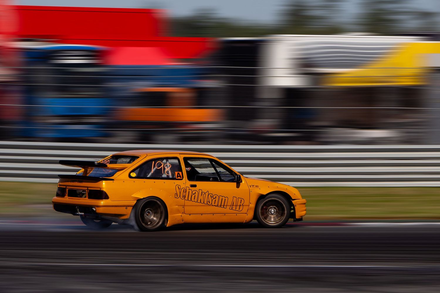 Orange race car speeds past blurred background during high-speed motorsport competition on track.
