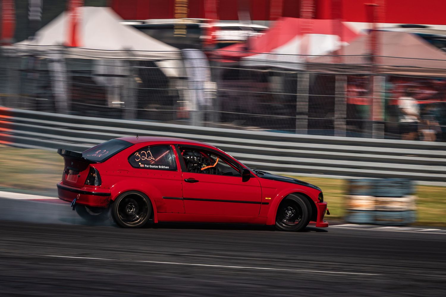 Red Honda Civic races on a track during a drifting event with motion blur and tents in the background.