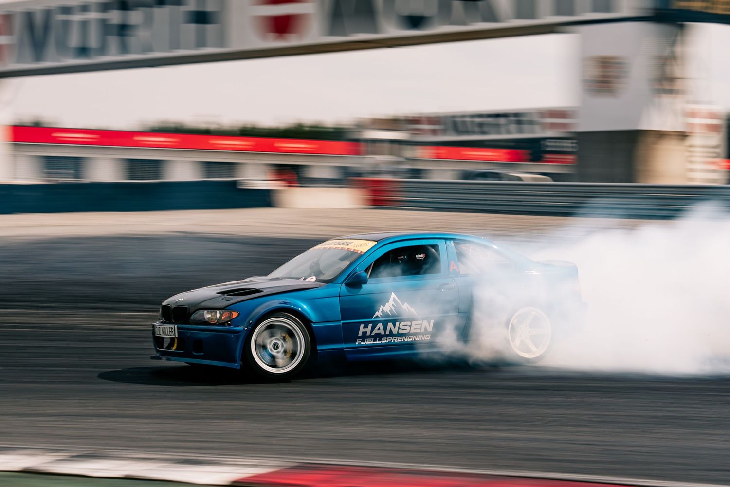 A blue sports car drifting on a race track with smoke billowing from its tires during a performance run.