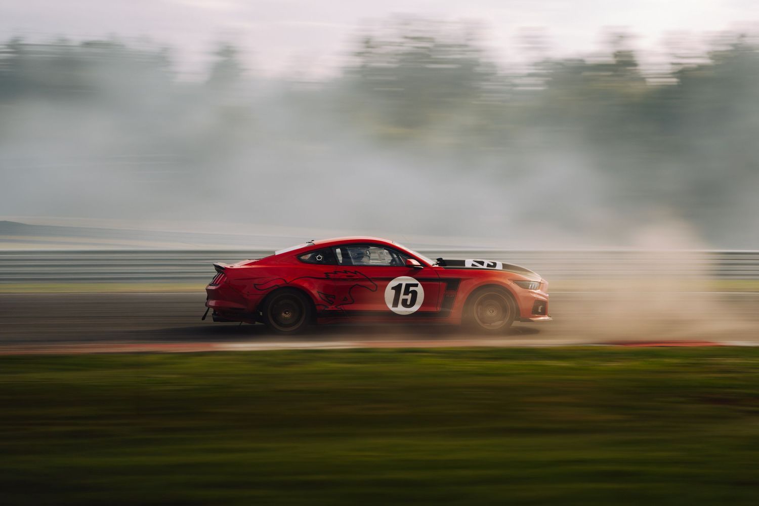 A red sports car drifts through a misty track creating dramatic tire smoke during a racing event.