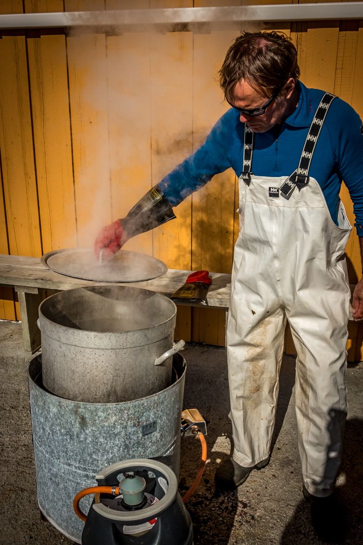 Cook in white overalls tending to steaming pots over an outdoor burner system.