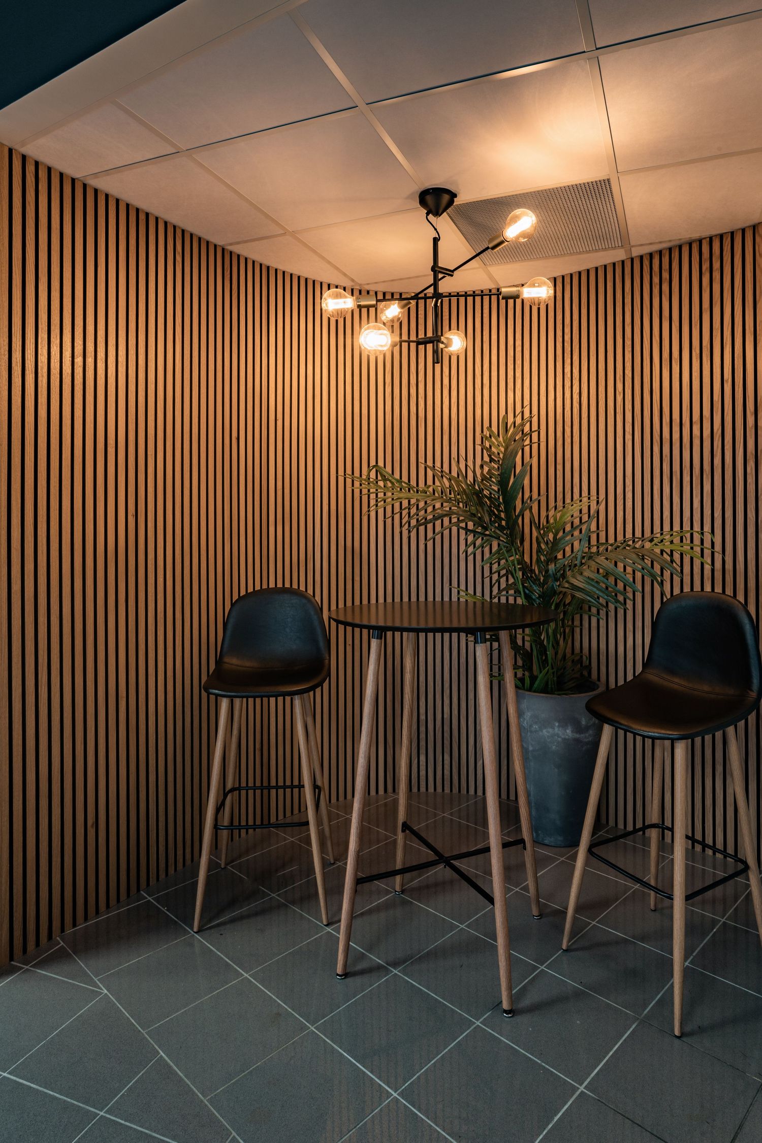 Modern bistro corner with vertical wood slats, pendant lighting, and tall bar seating arrangement.
