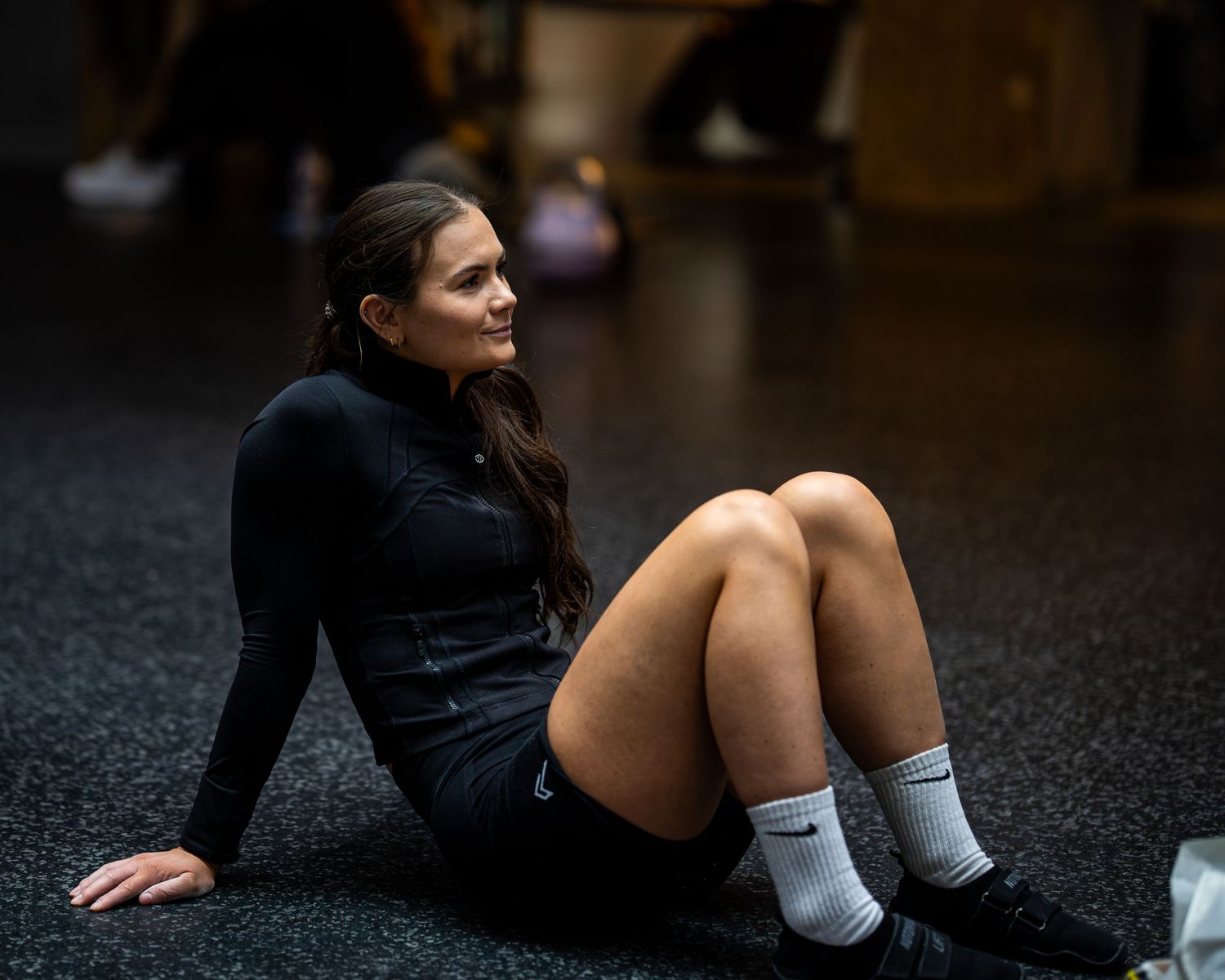 Athlete resting on gym floor wearing black athletic gear and white socks.