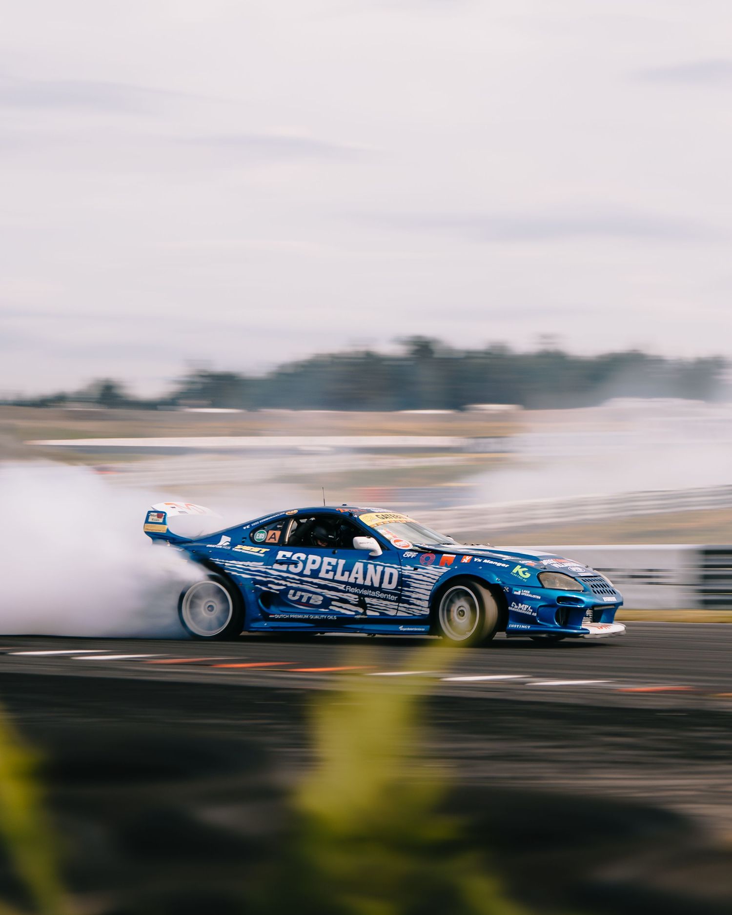 A blue drag racing car speeds past in a motion-blurred action shot on a racetrack.