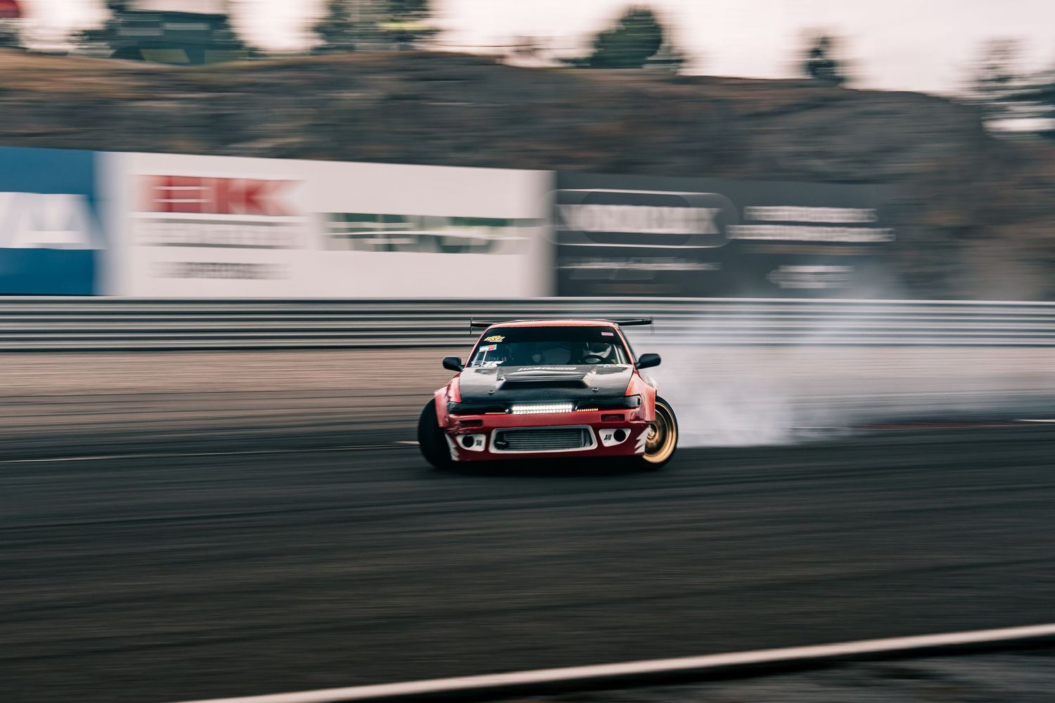 Red and black sports car drifting on a racetrack with smoke trailing behind it during competition.