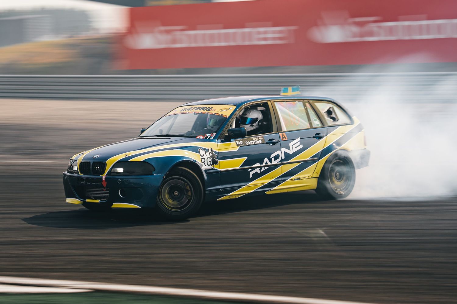 A sequence of drift racing cars performing synchronized drifting maneuvers on a racetrack with tire smoke trailing behind.