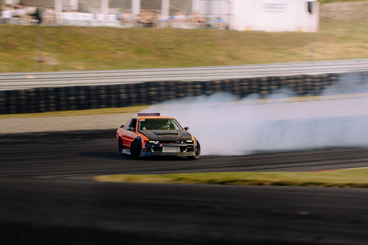 A race car drifts around a track corner with smoke billowing from its tires during a motorsport competition.