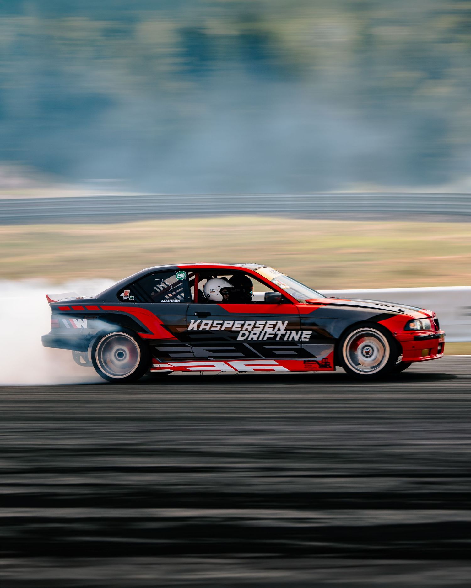 Professional drift car performing a dramatic sideways slide with tire smoke on a racing circuit.