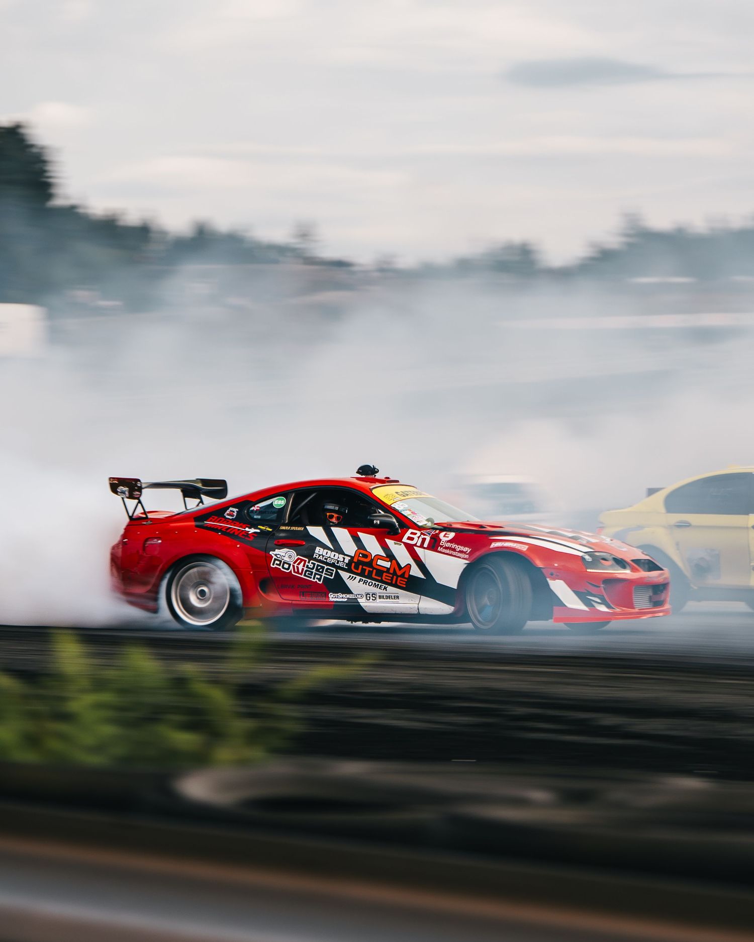 Red drift car creating smoke while drifting on track during motorsport competition.