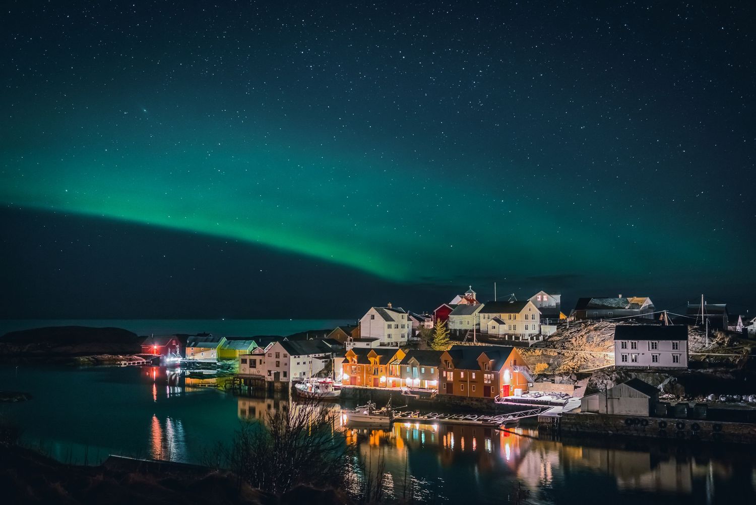 Aurora borealis illuminates the night sky above a colorful fishing village on the water.
