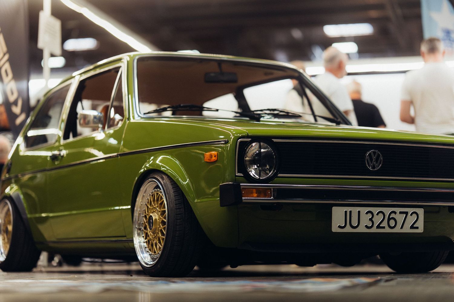 Side profile of a lowered vintage green car with custom wheels in parking garage lighting.