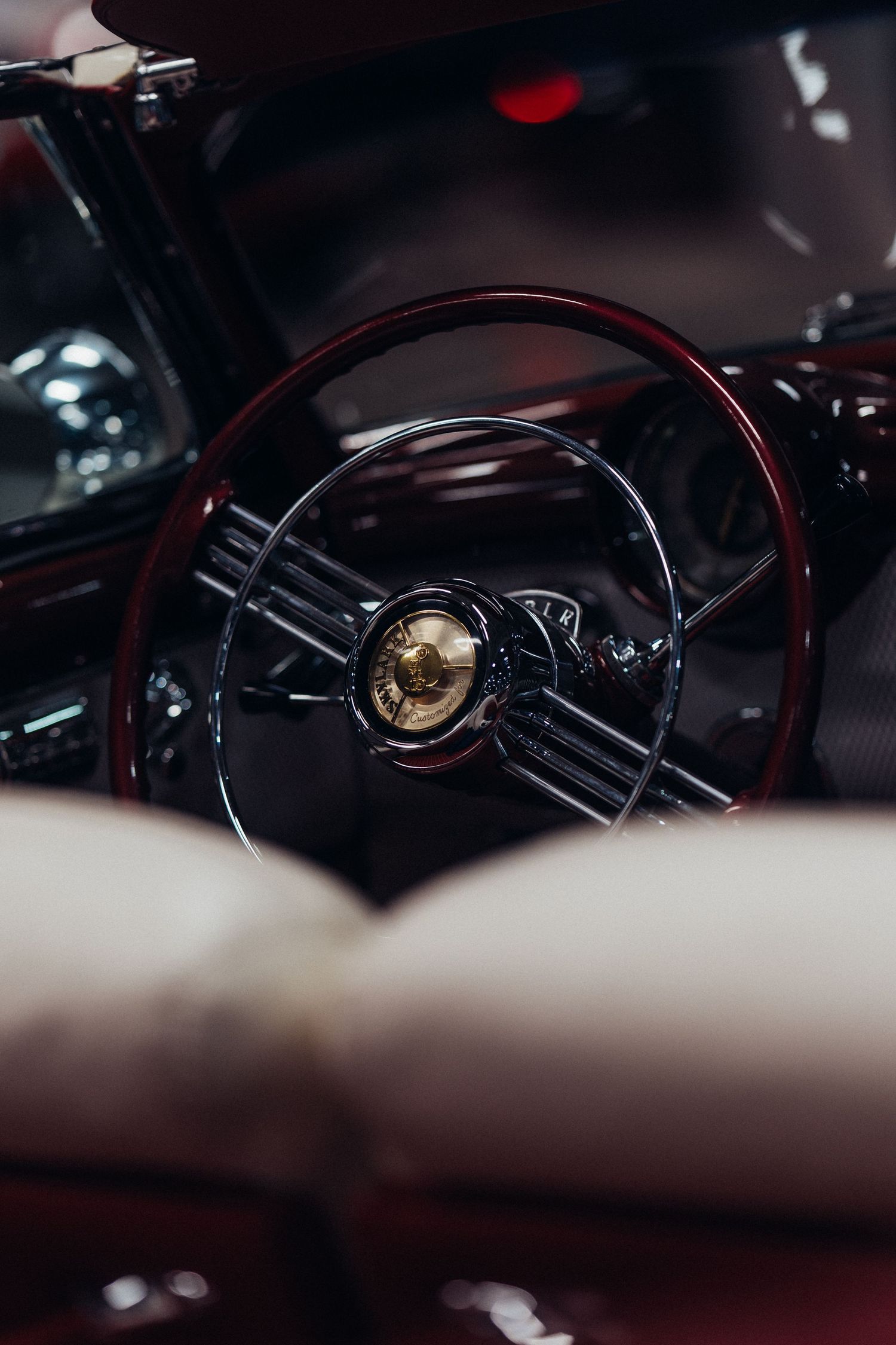 Close-up view of a vintage car steering wheel with chrome details and wood trim in dark lighting.