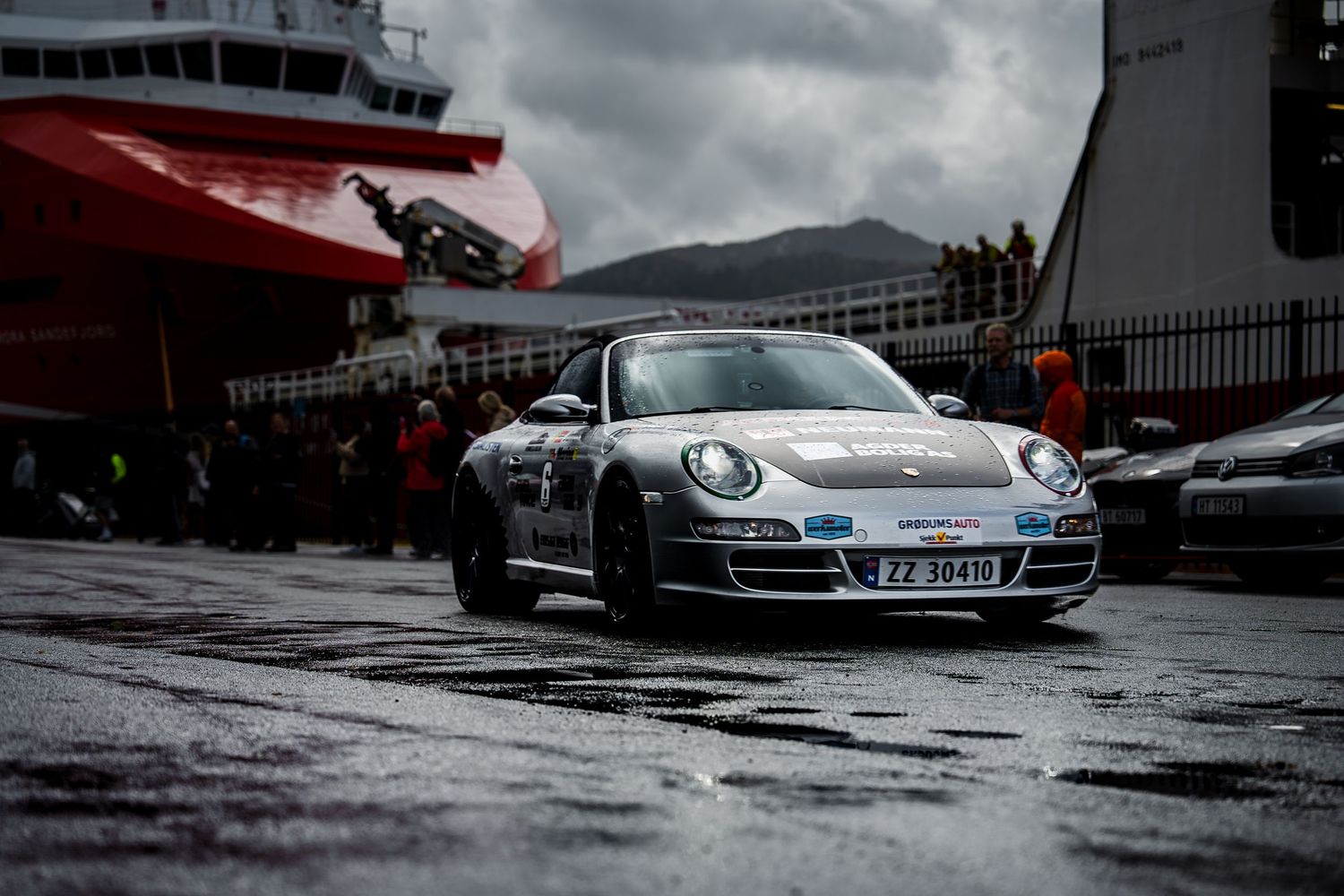 High-end sports cars displayed in rainy conditions with dramatic dark clouds overhead.