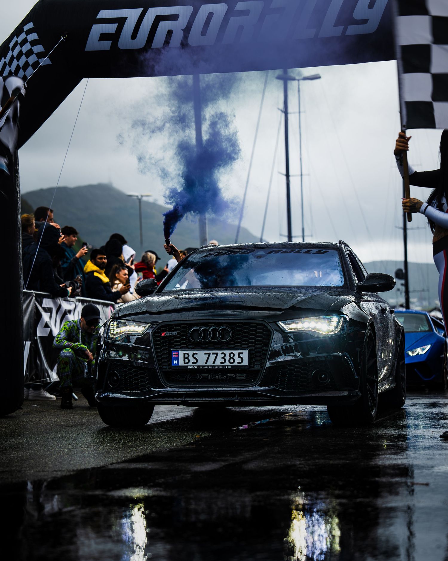Black Audi RS crossing finish line under Eurorally arch with blue smoke in background.