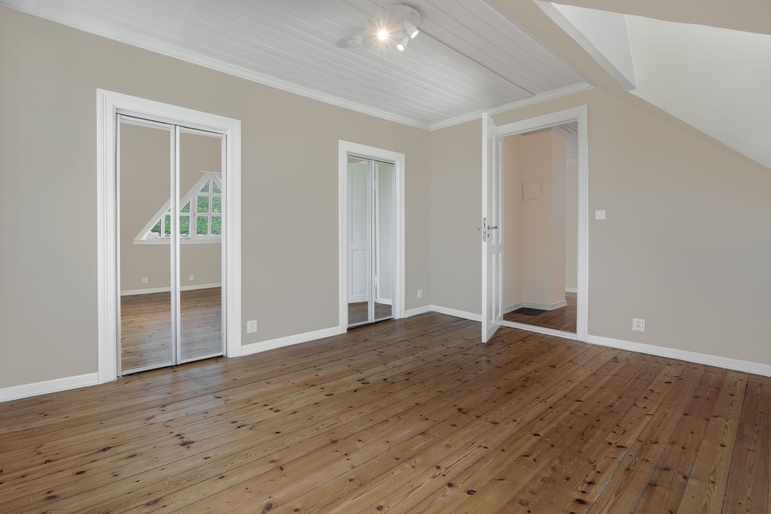 Modern bedroom with wooden floors, white crown molding, and multiple doorways in beige walls.