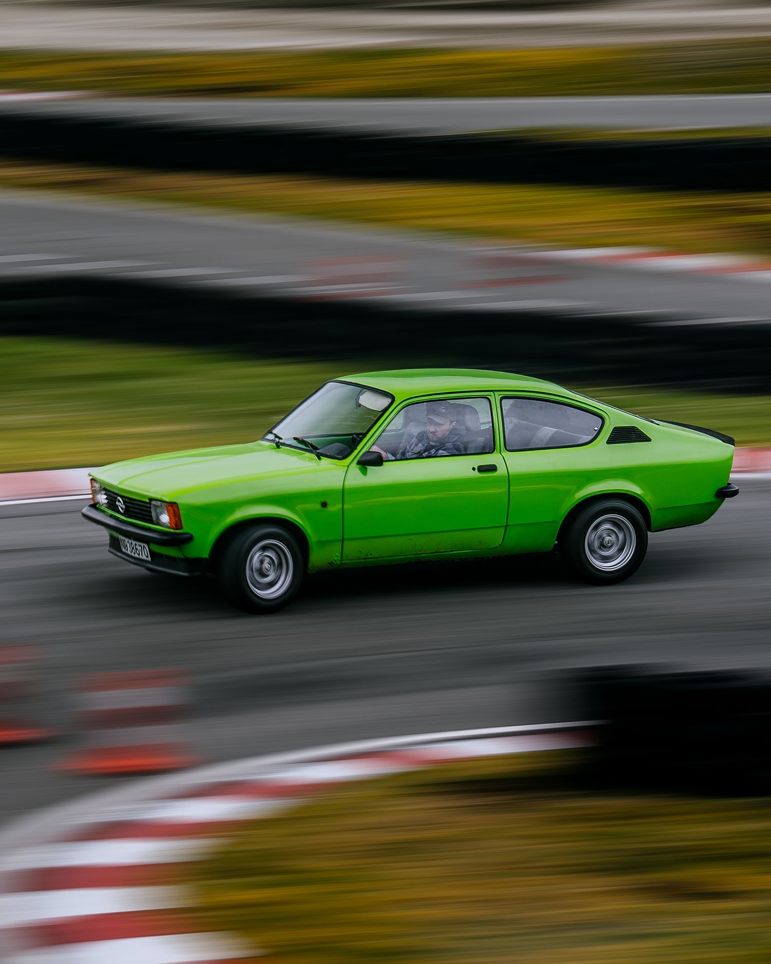 A bright green vintage sports car in motion creates a dynamic motion blur effect on a racetrack.