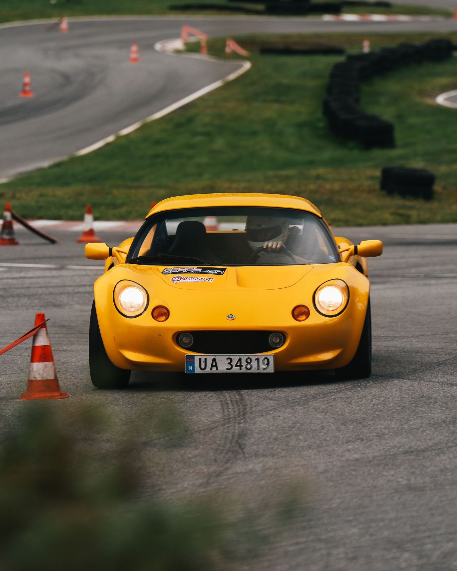 Yellow Lotus Elise sports car navigating a race track course marked with orange traffic cones.