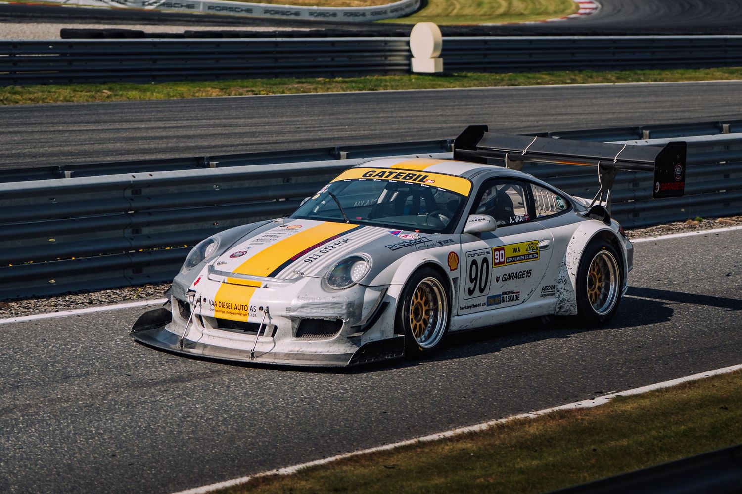 Racing car with yellow and white livery speeds around a racetrack during a motorsport competition.